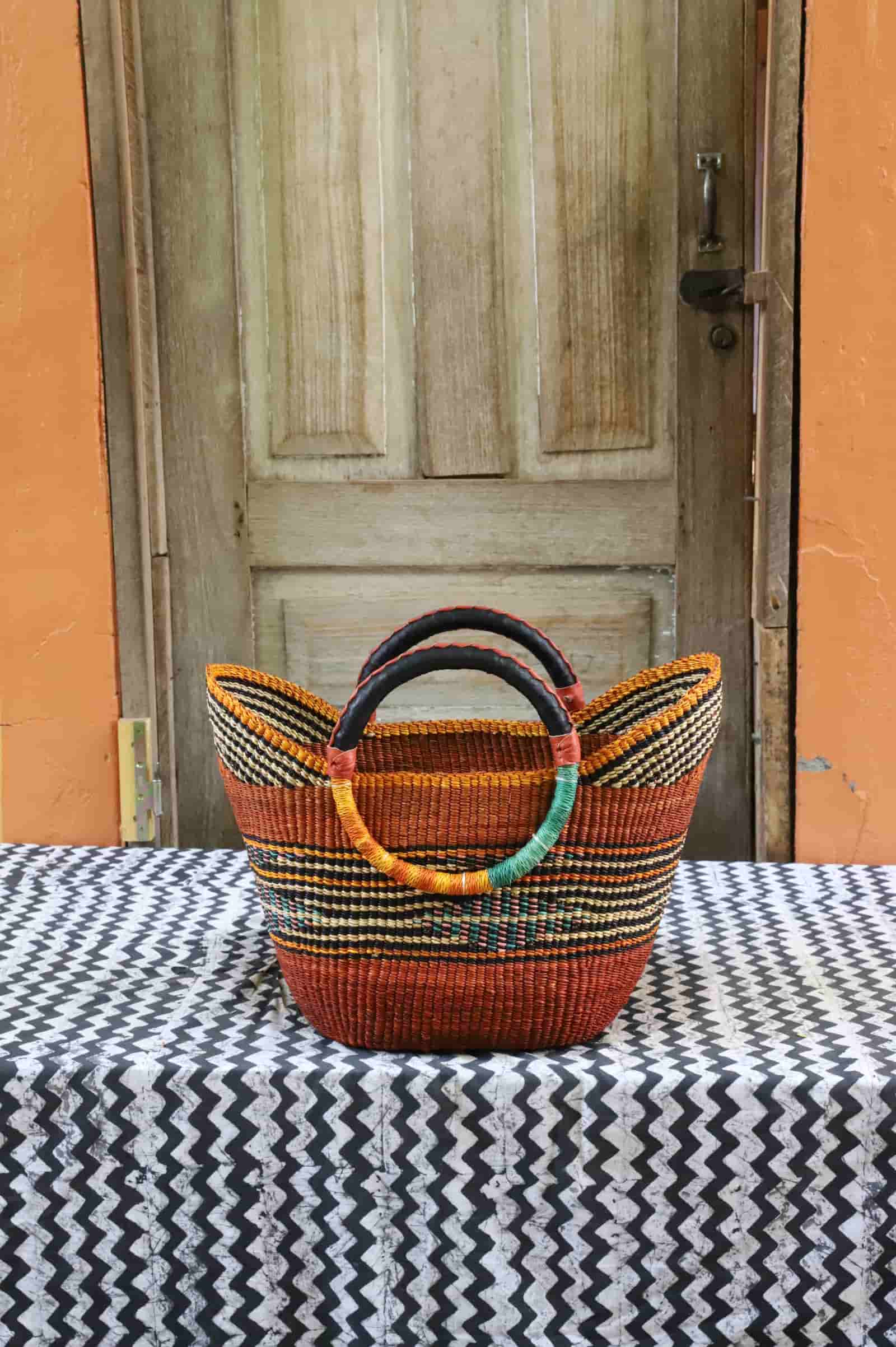 Woven basket with colorful handles on a tablecloth in front of a wooden door.