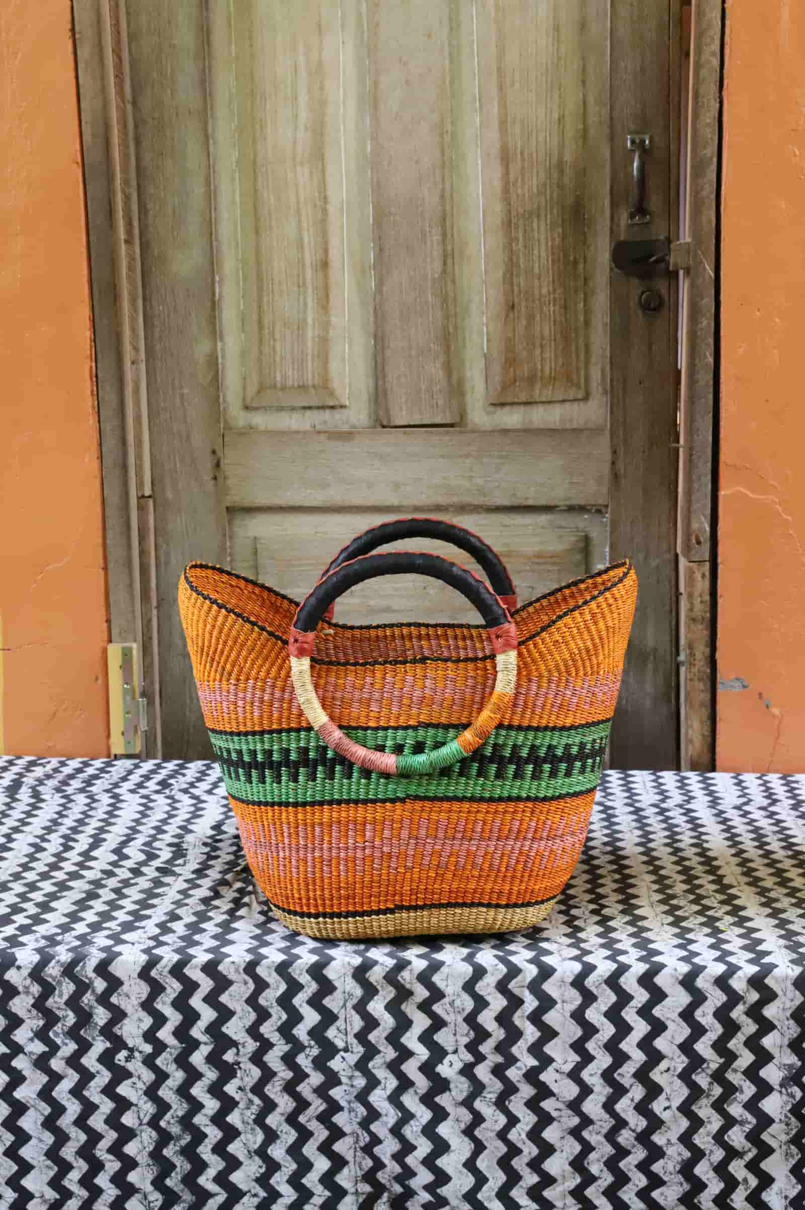 Woven beach bag in orange and terracotta with a green and black stripe band and circular leather handles