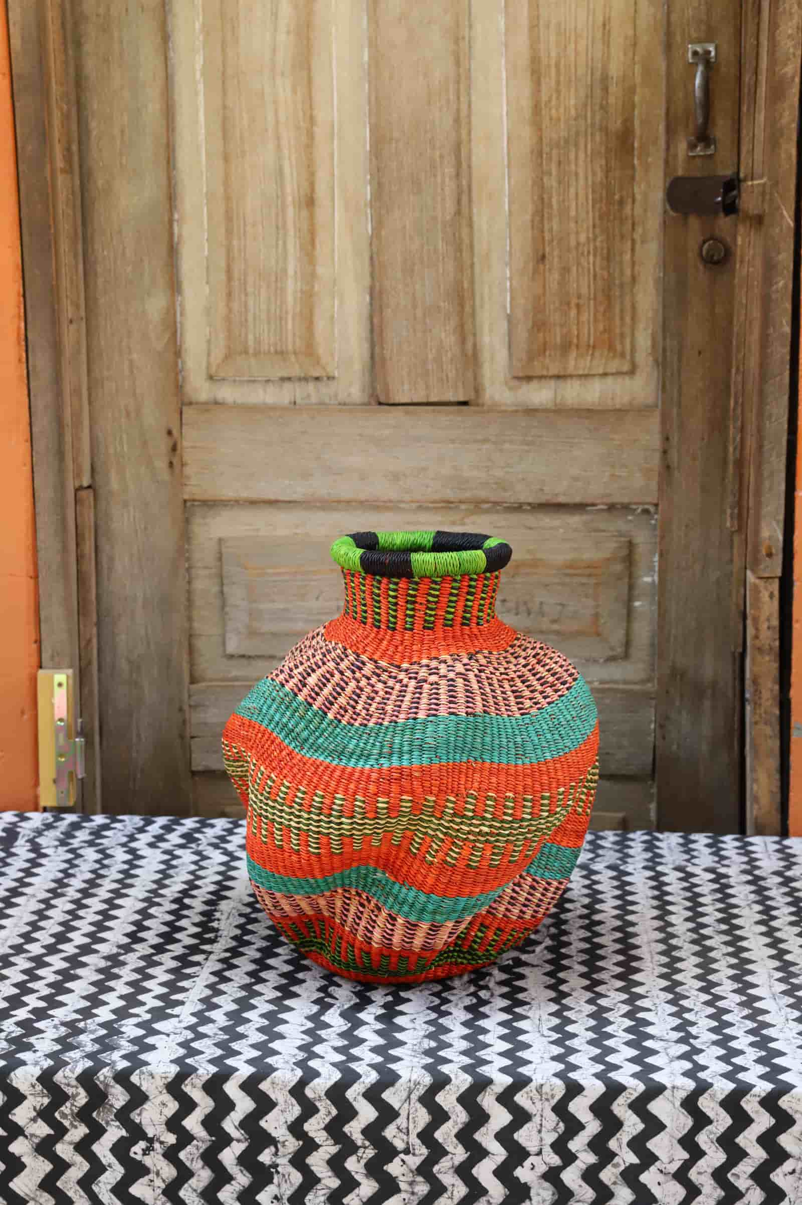 Colorful woven piece on a black and white patterned surface with a wooden door in the background.