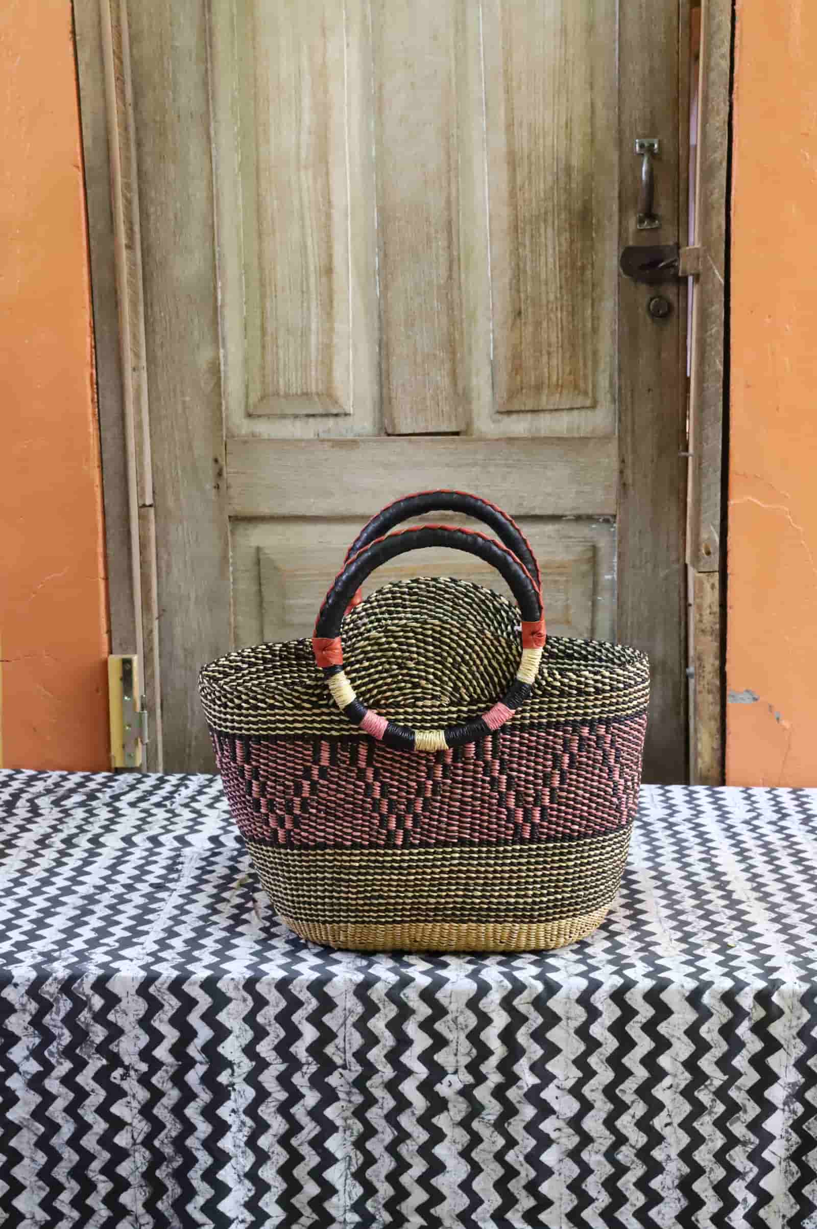 Colorful woven carry on bag with premium leather handles on a black and white cloth against a wooden door.