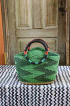 Green woven basket with black handle on a tablecloth in front of a wooden door.