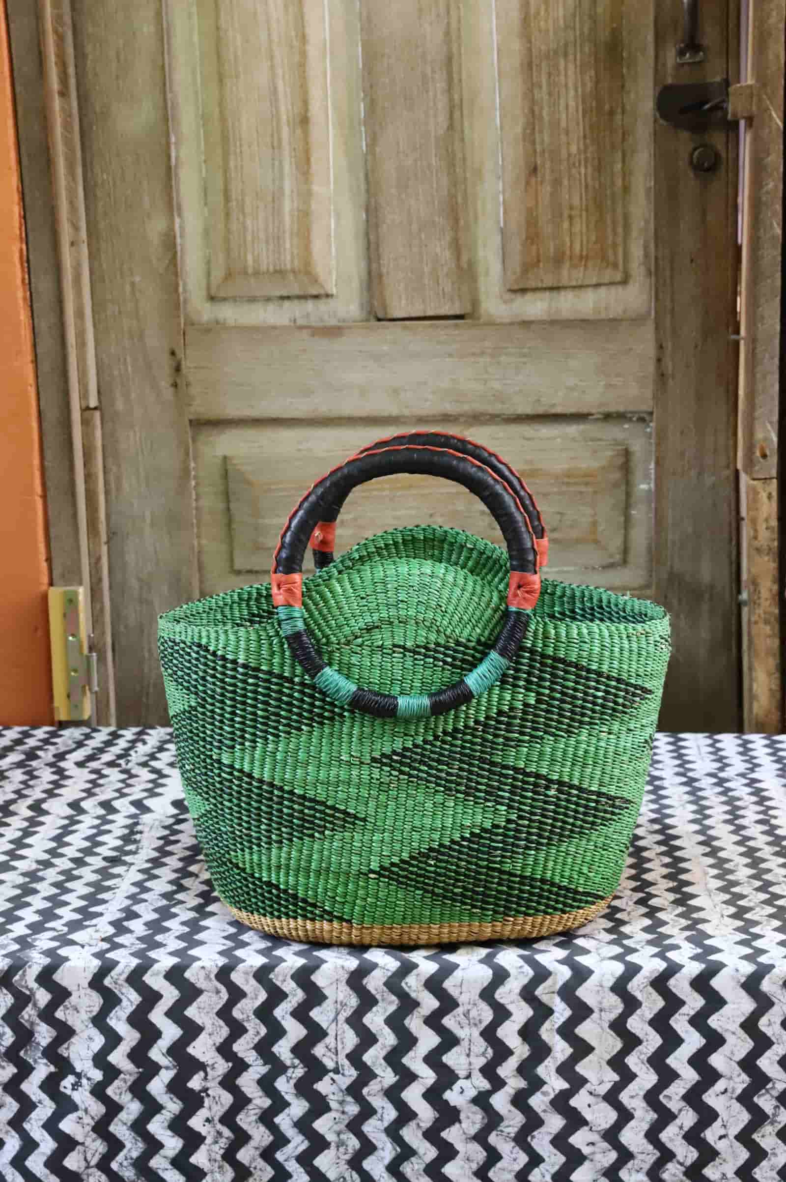 Green woven basket with black handle on a tablecloth in front of a wooden door.