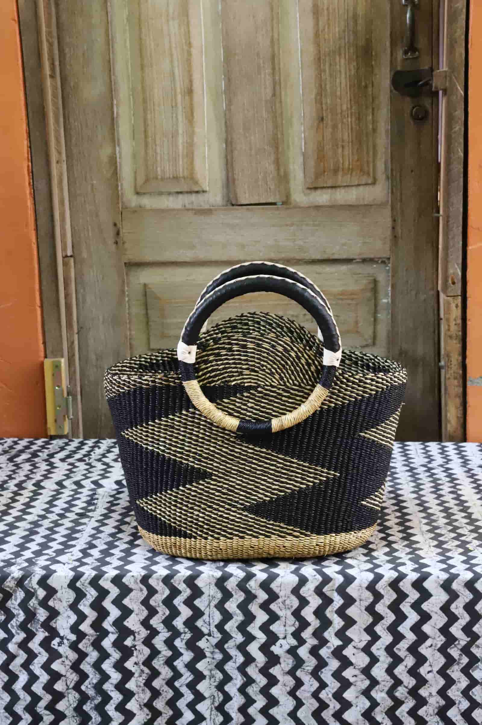 Colorful woven carry on bag with premium leather handles on a black and white cloth against a wooden door.