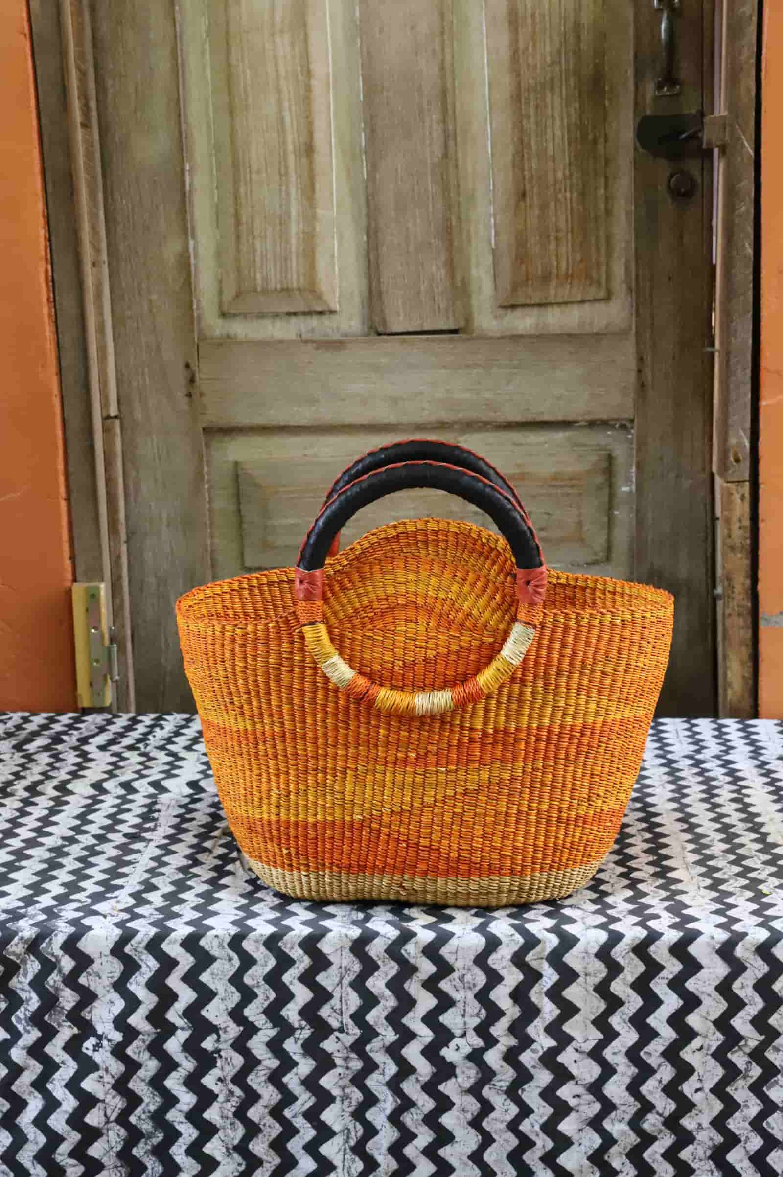 Colorful woven carry on bag with premium leather handles on a black and white cloth against a wooden door.