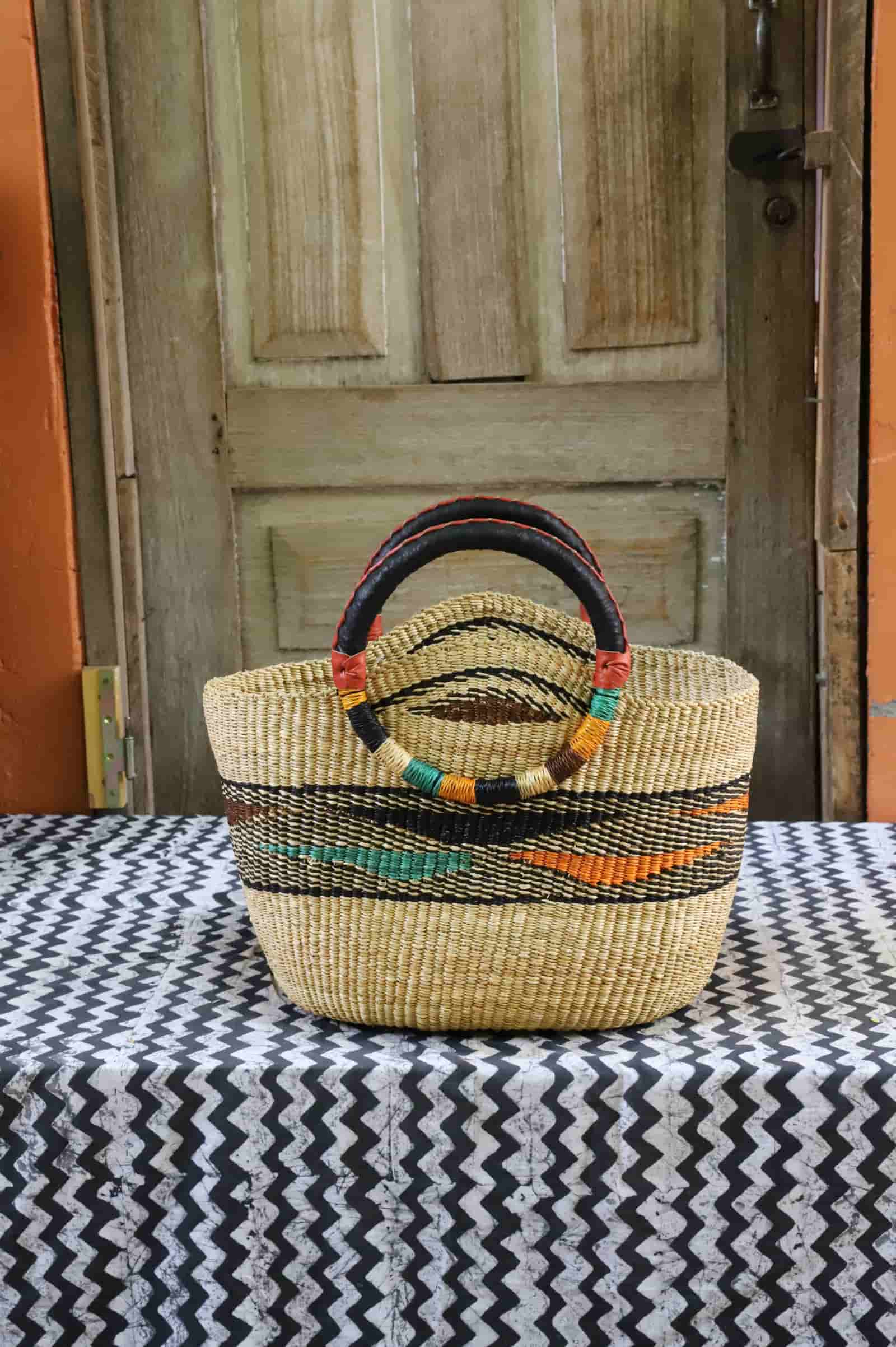 Colorful woven carry on bag with premium leather handles on a black and white cloth against a wooden door.