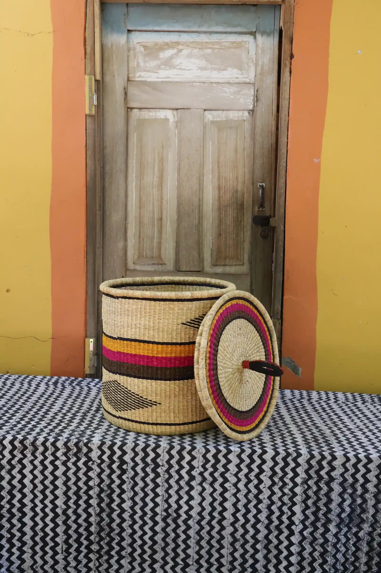 Handwoven Bolga laundry basket with lid removed, natural body with pink and orange bands and matching lid.