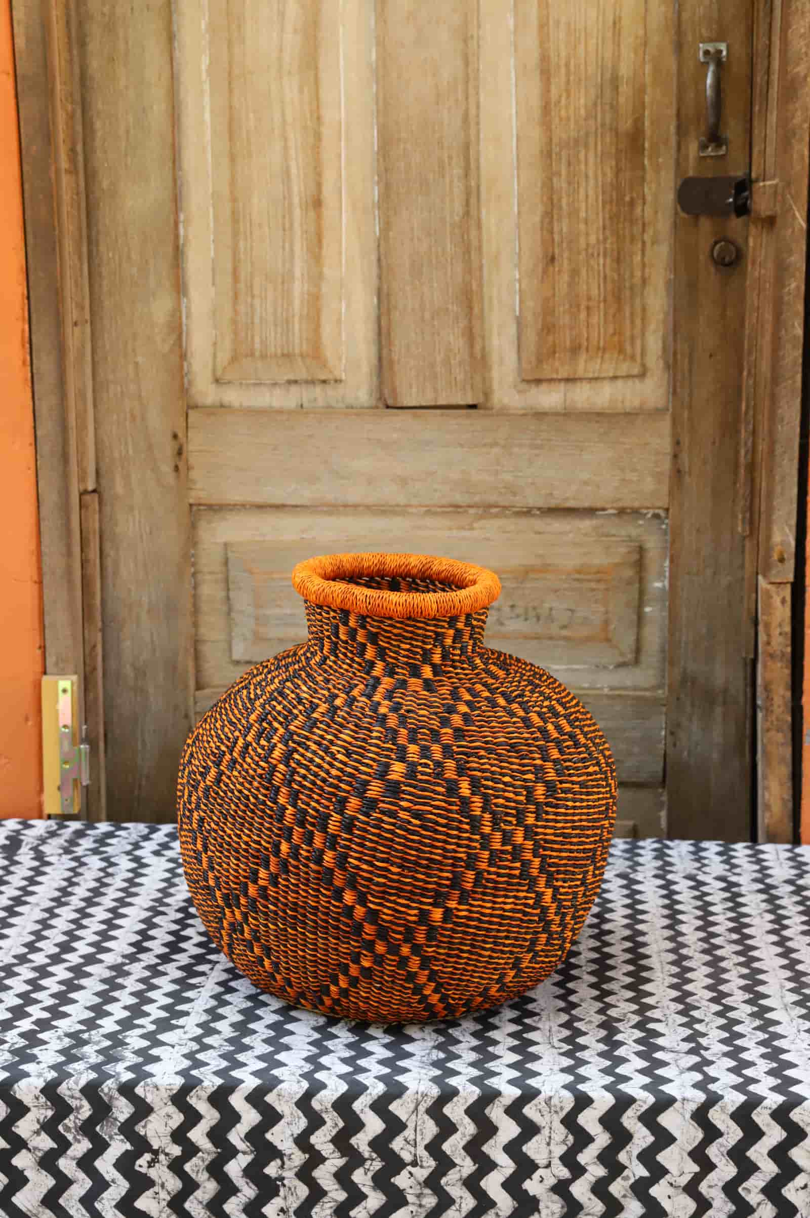 Decorative handwoven basket with colorful patterns on a black and white cloth against a wooden door.