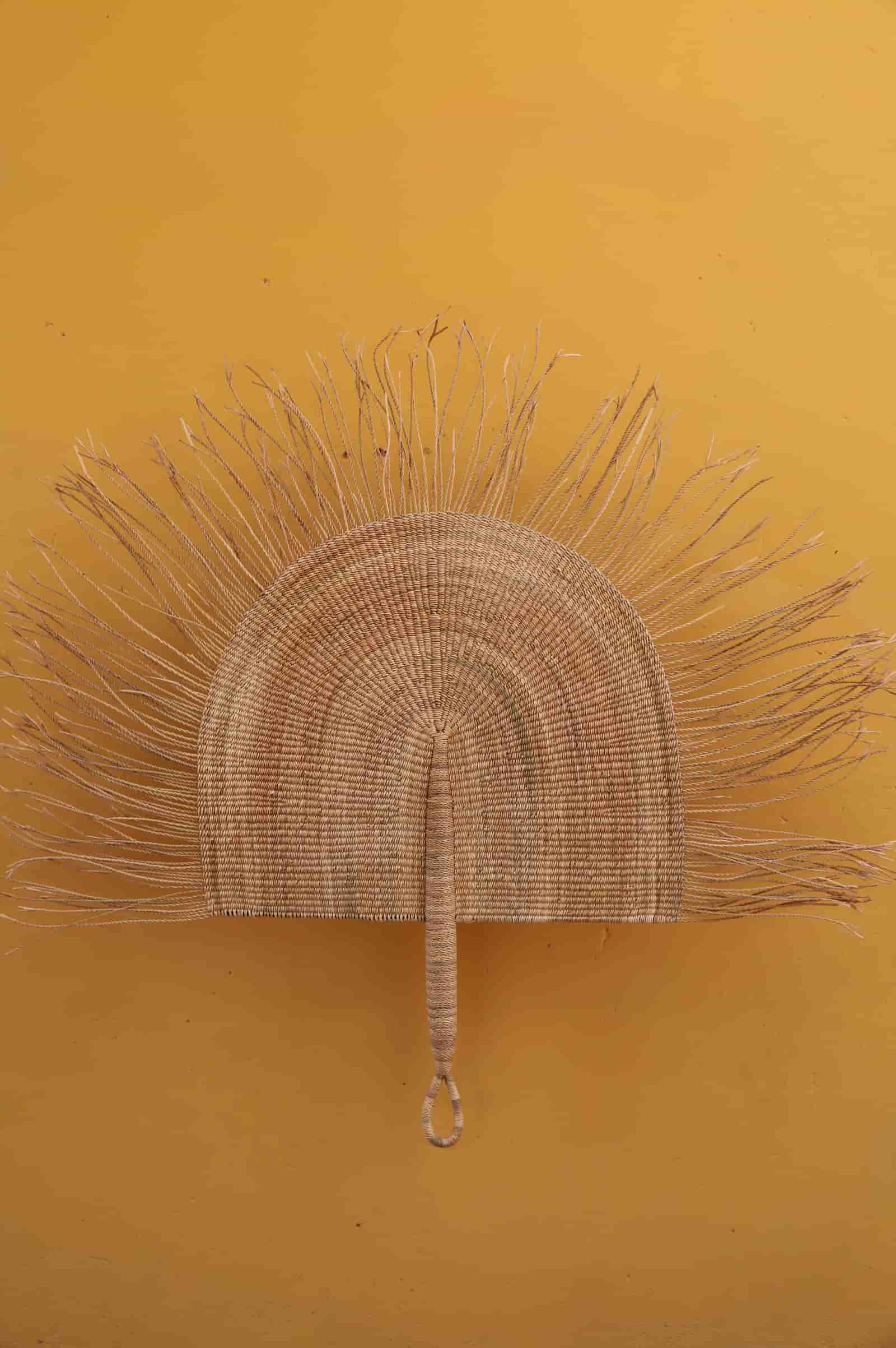 Decorative metal fan with a handle on a mustard yellow background