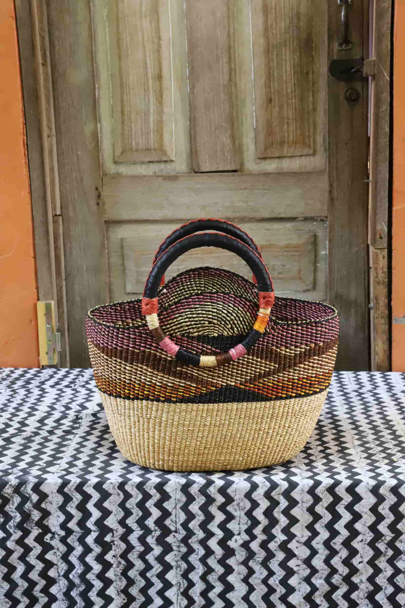 Colorful woven carry on bag with premium leather handles on a black and white cloth against a wooden door.