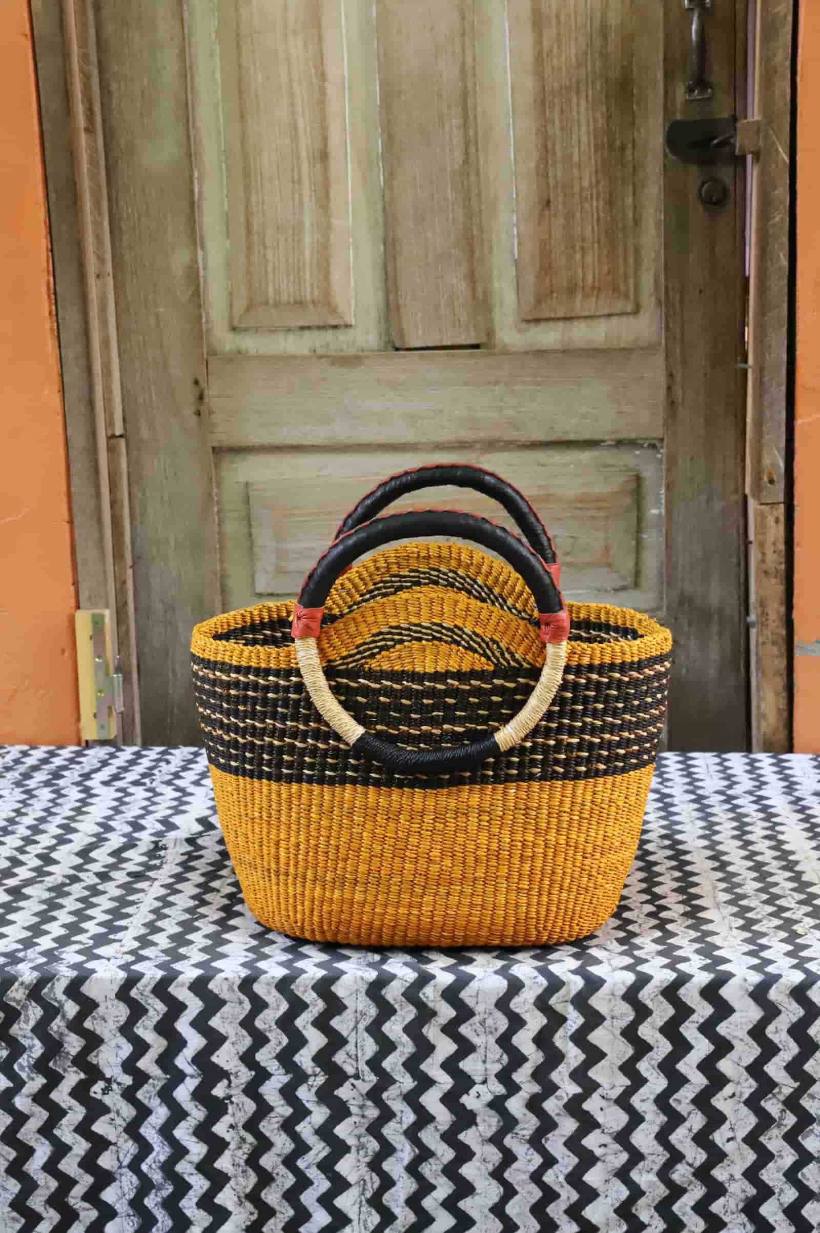 Colorful woven carry on bag with premium leather handles on a black and white cloth against a wooden door.