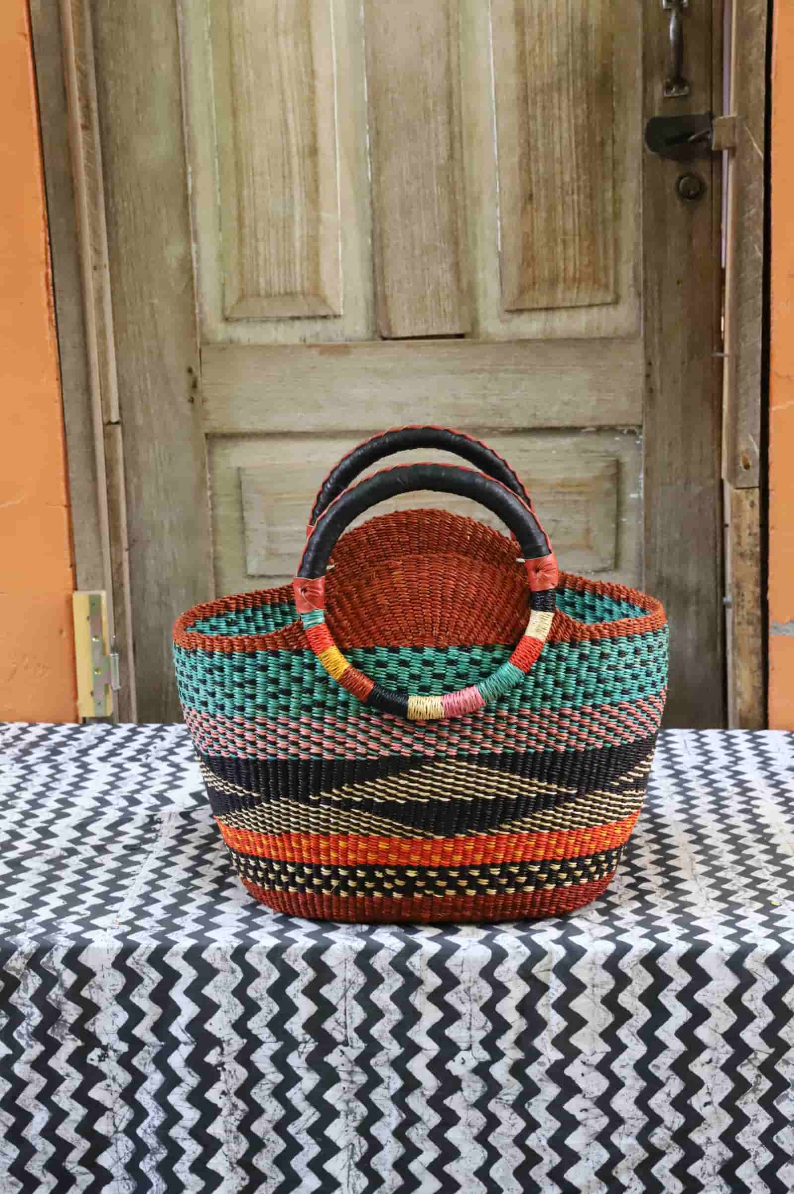 Colorful woven carry on bag with premium leather handles on a black and white cloth against a wooden door.