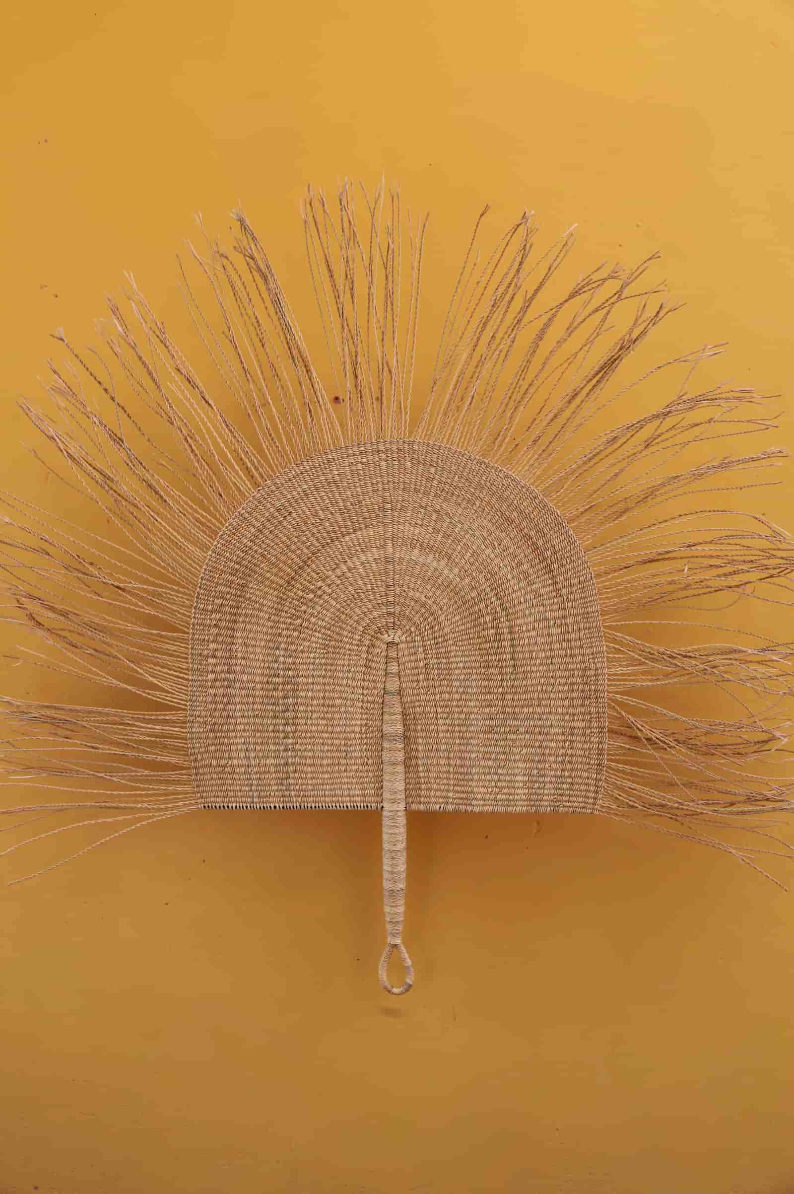 Woven fan with straw-like bristles on a yellow background