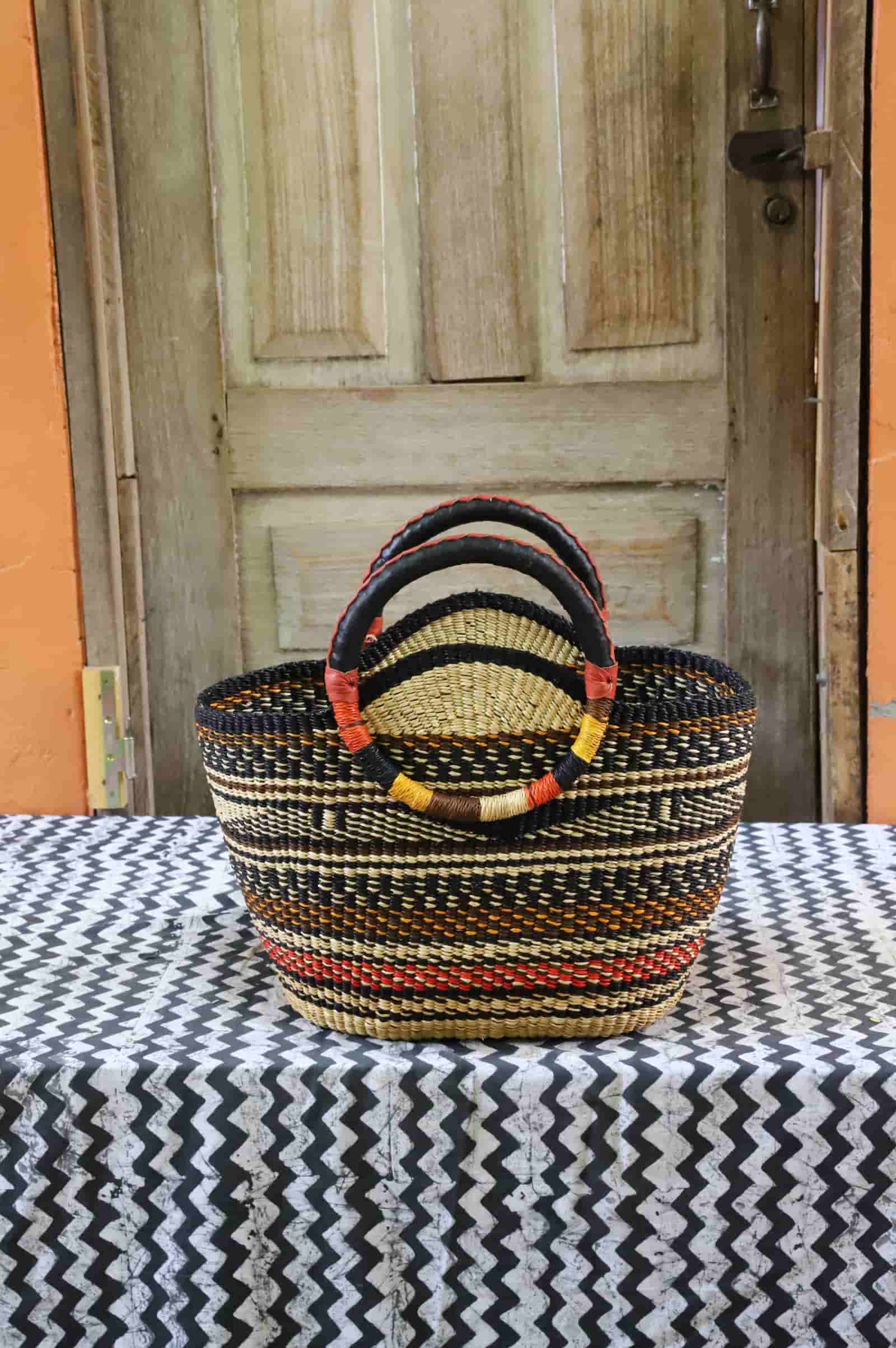 Colorful woven carry on bag with premium leather handles on a black and white cloth against a wooden door.