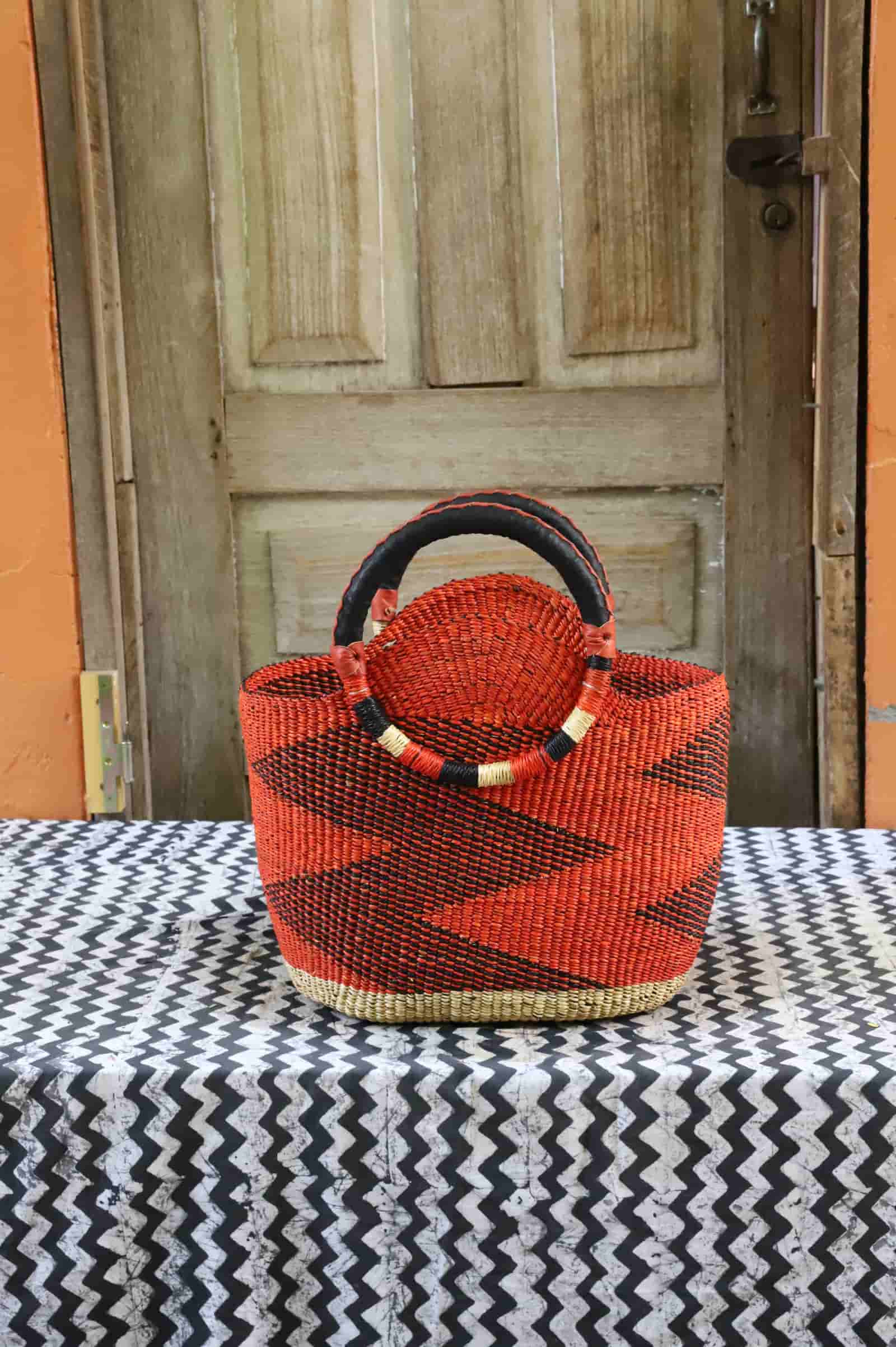 Colorful woven carry on bag with premium leather handles on a black and white cloth against a wooden door.
