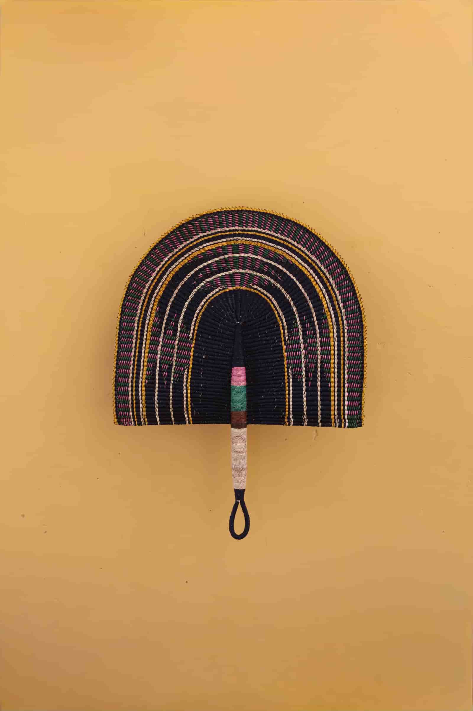 Decorative  woven wall art with a colorful handle on a yellow background