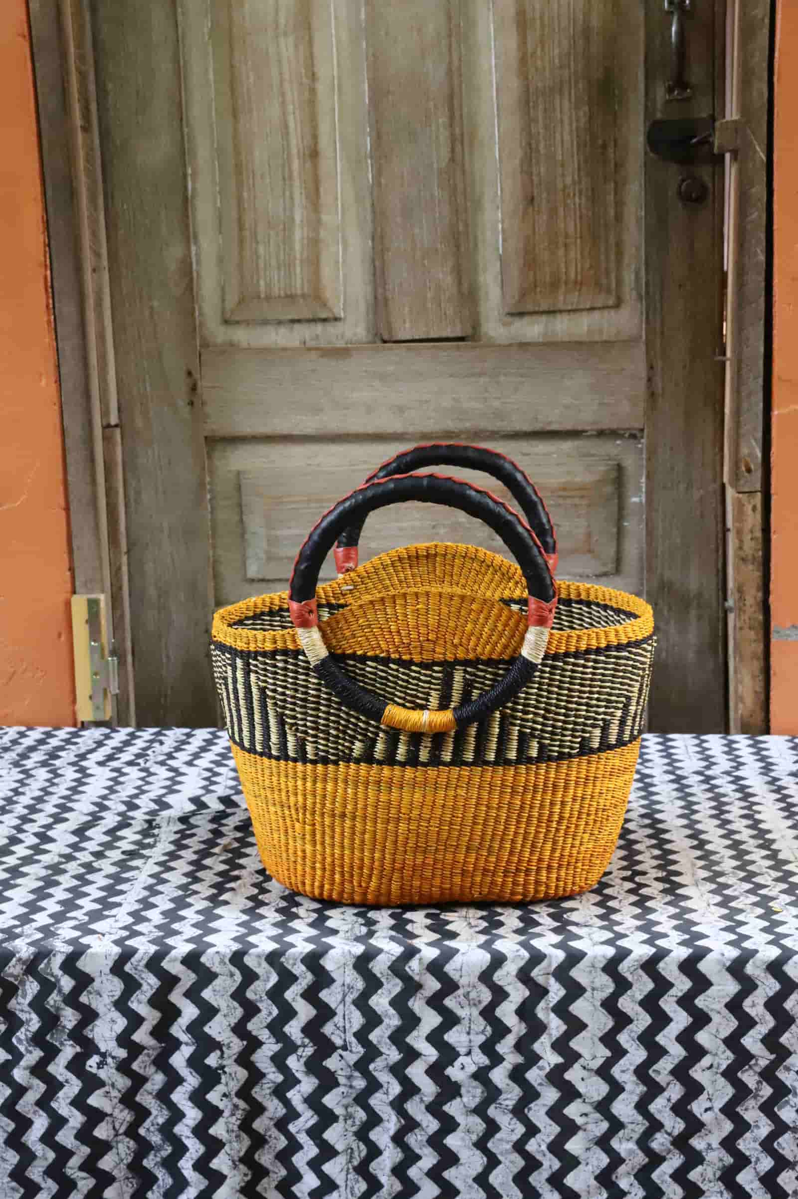 Colorful woven carry on bag with premium leather handles on a black and white cloth against a wooden door.