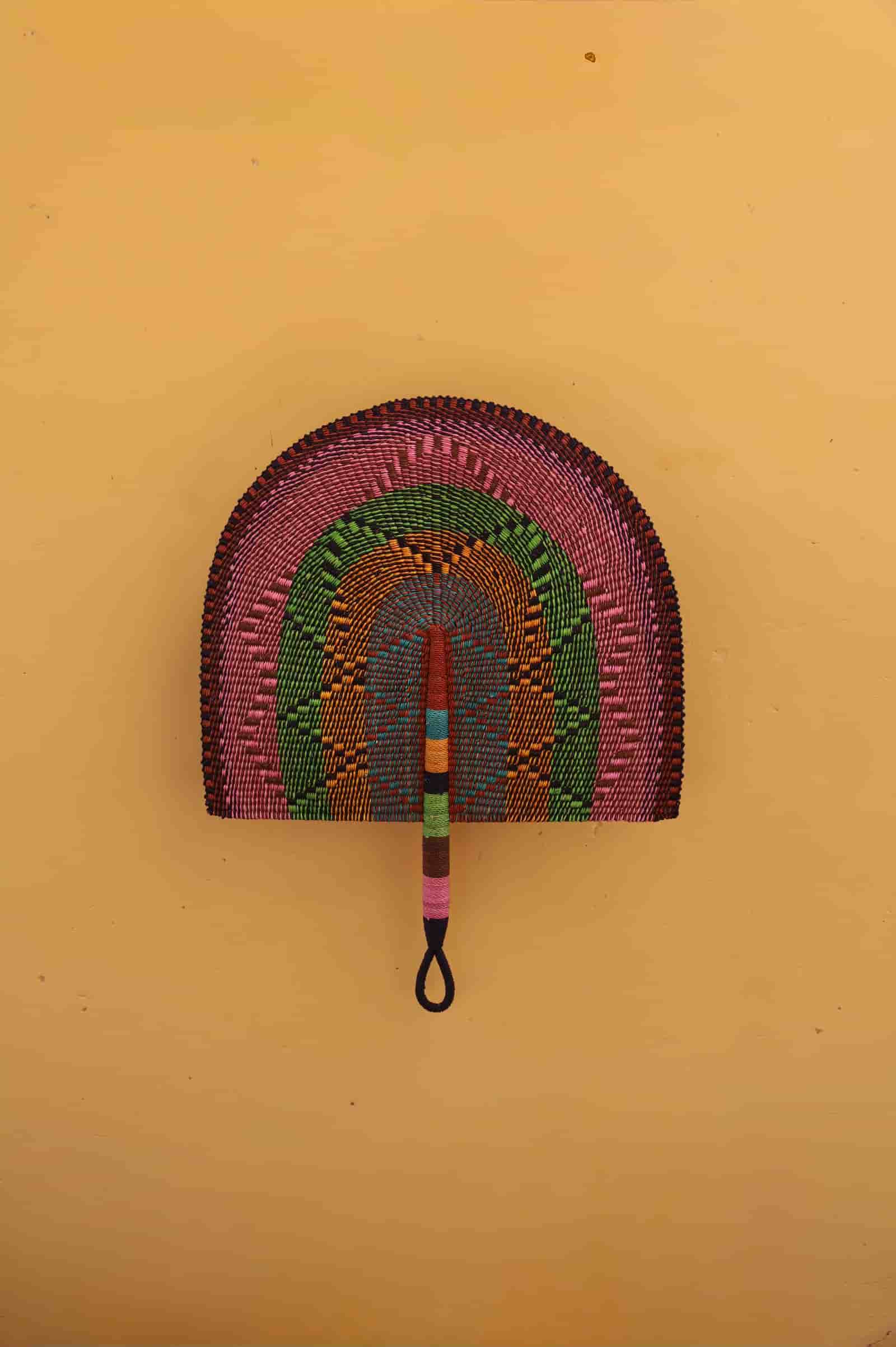 Colorful woven fan with a rainbow pattern on a yellow background