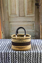 Woven basket with black handle on a patterned tablecloth in front of a wooden door.