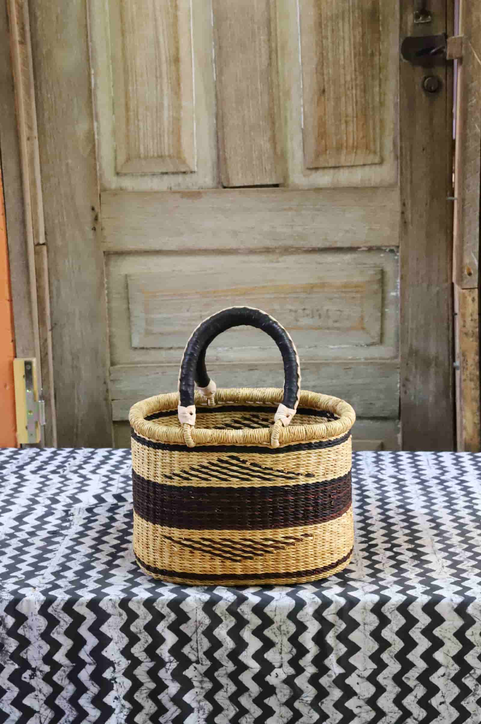 Woven basket with black handle on a patterned tablecloth in front of a wooden door.