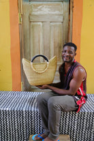 Man holding a woven basket in front of a yellow wall and wooden door.