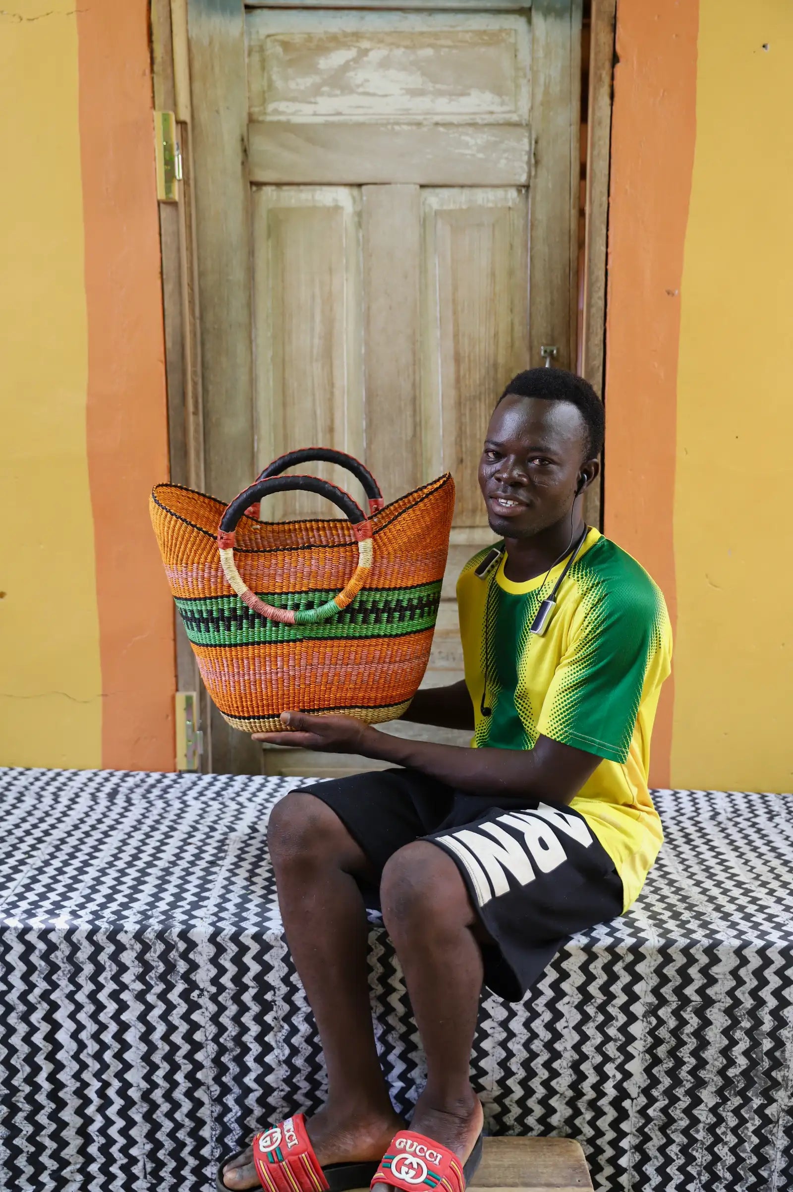 Young man in green and yellow jersey holding a woven orange beach bag with green stripe