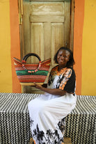 Woman holding a colorful woven basket in front of a wooden door with a yellow wall.