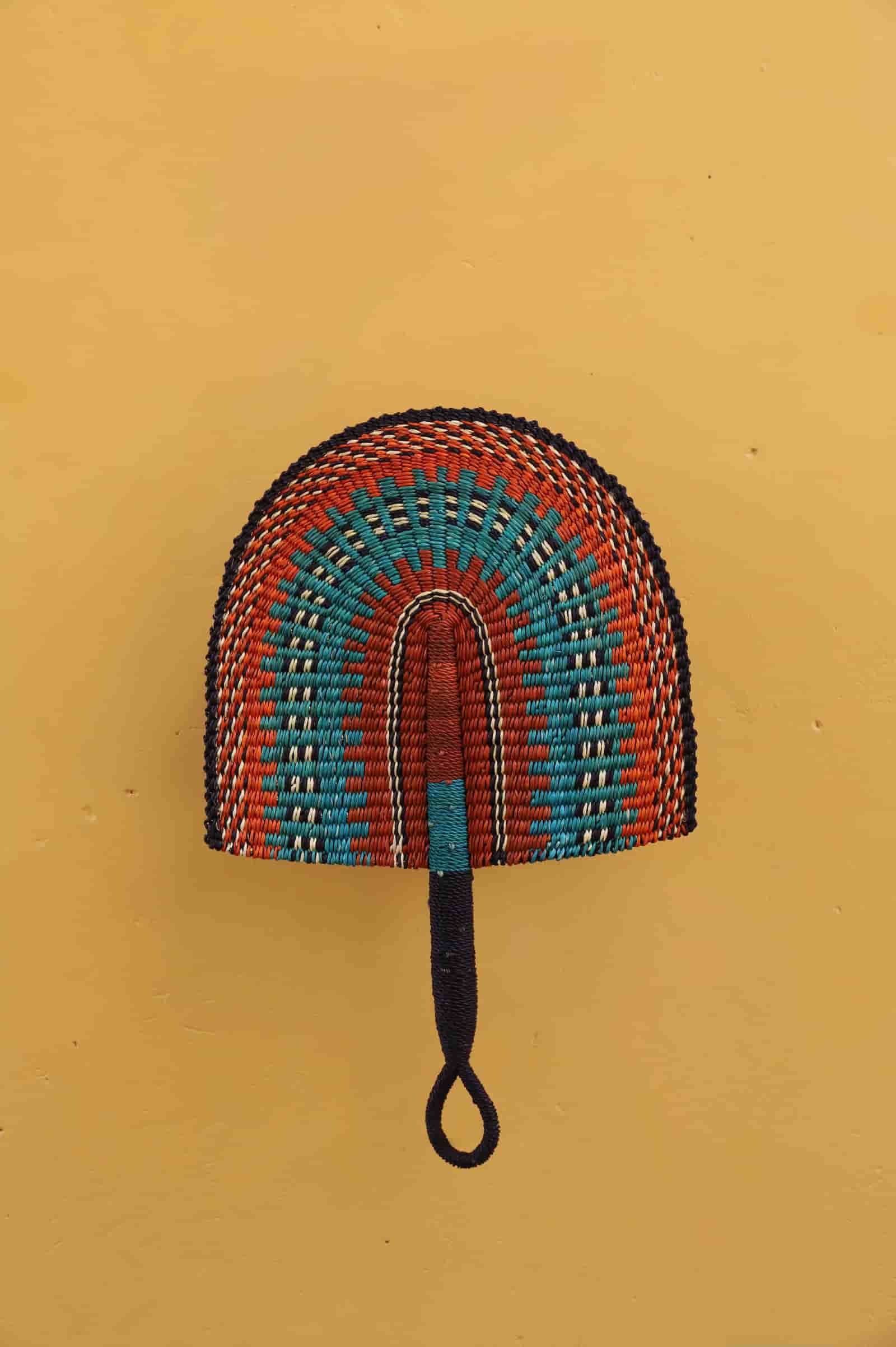 Woven hand fan with a handle on a yellow background