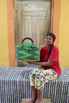 Woman holding a green woven handbag in front of a wooden door.