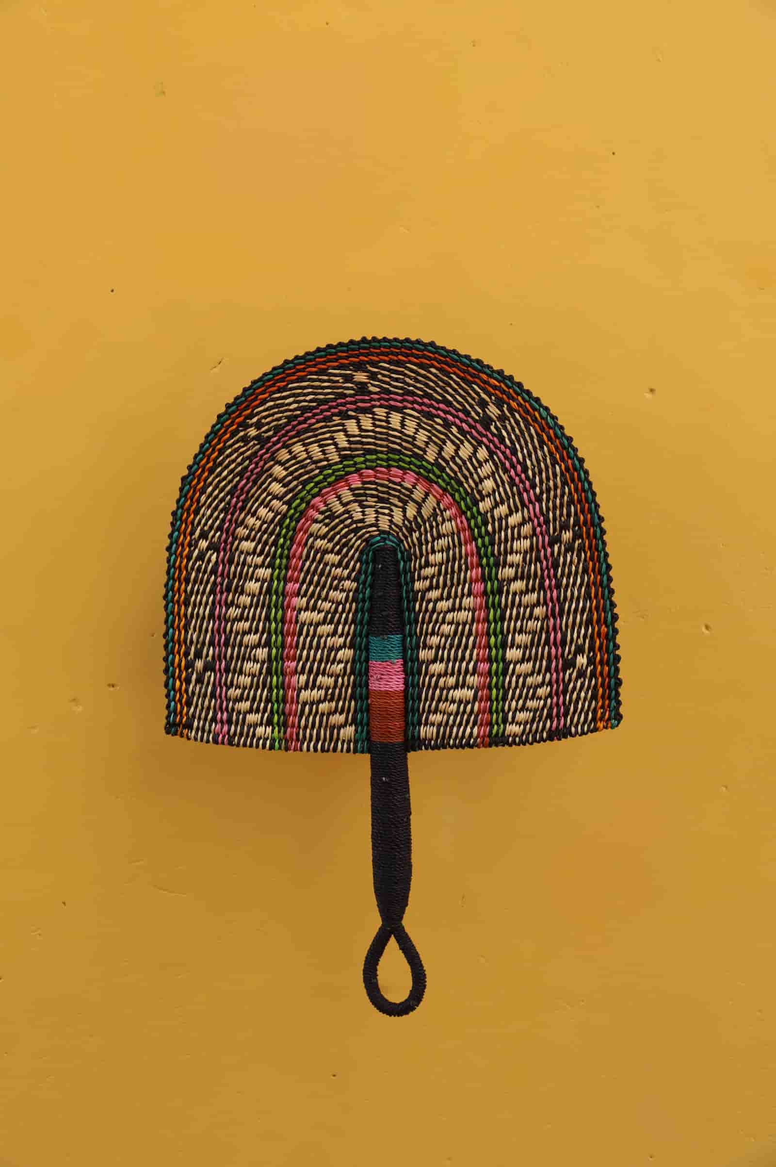 Woven fan with a handle on a mustard yellow background