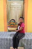 Person holding a colorful woven basket in front of a wooden door with a yellow wall.