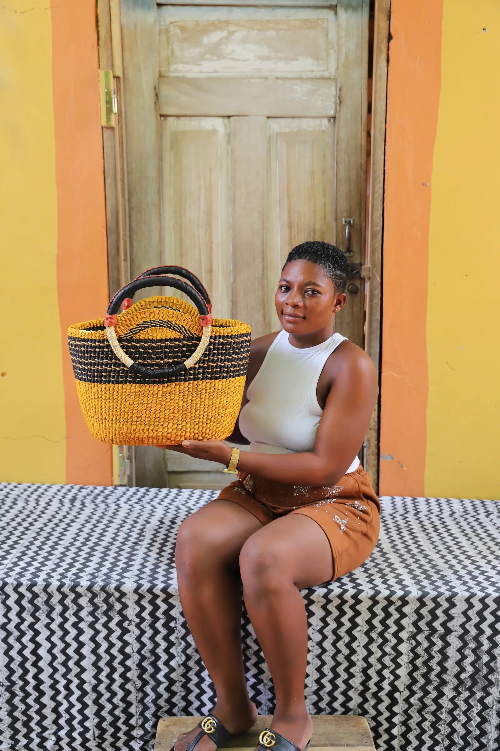 Artisan holding a colorful woven carry on bag with premium leather handles on a black and white cloth against a wooden door.