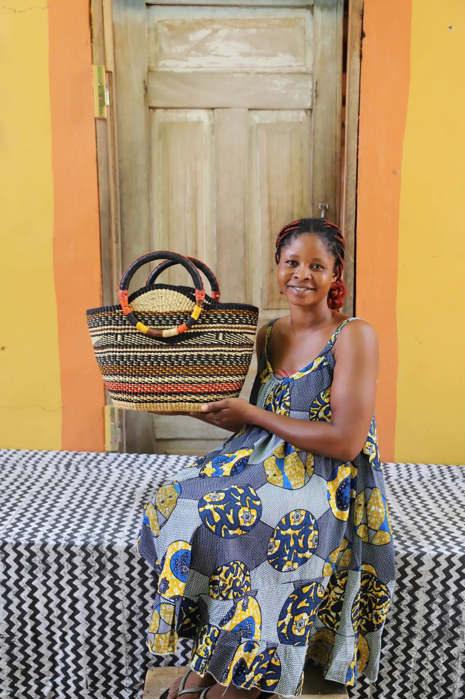 Artisan holding a colorful woven carry on bag with premium leather handles on a black and white cloth against a wooden door.