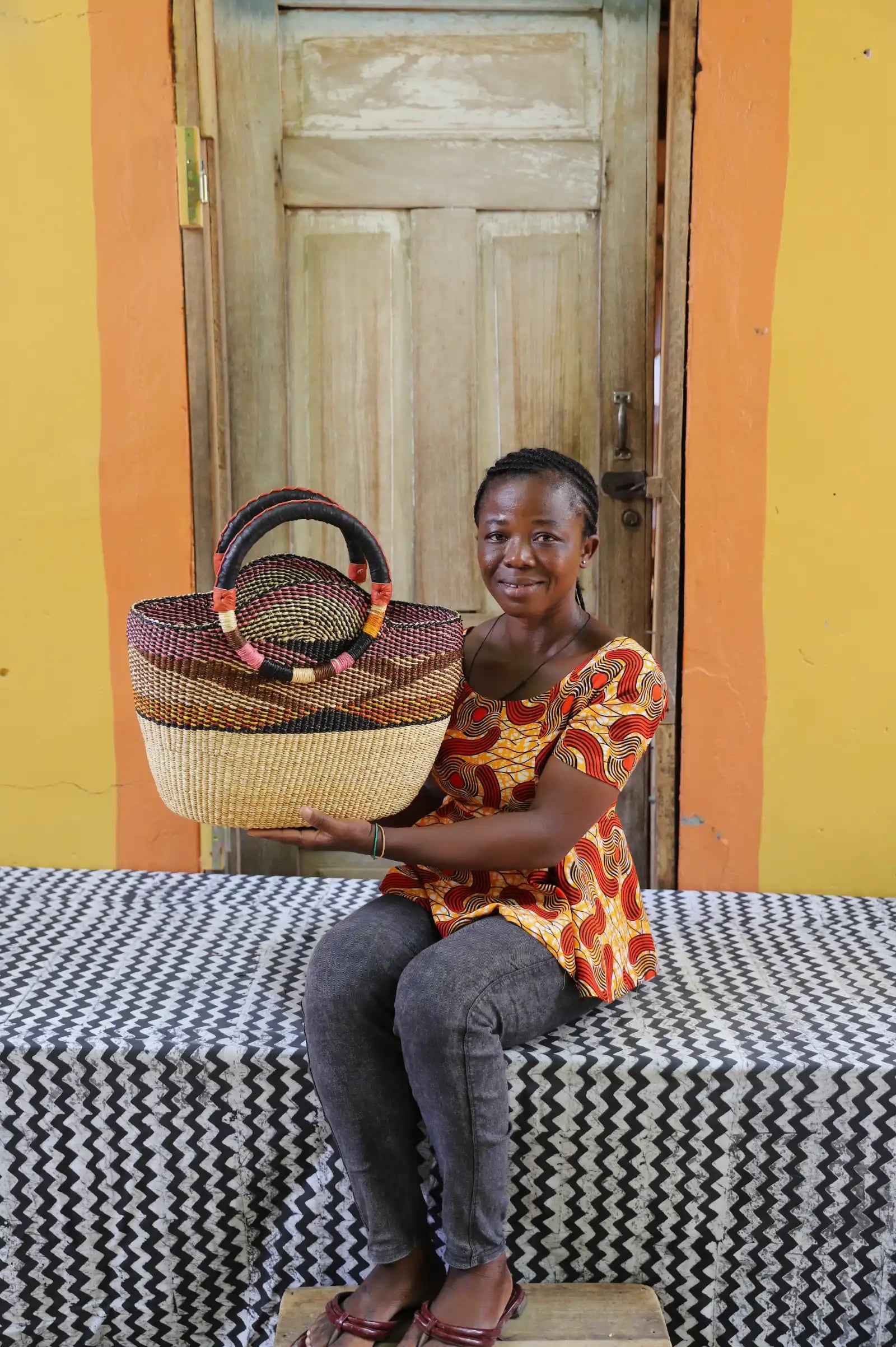 Artisan holding a colorful woven carry on bag with premium leather handles on a black and white cloth against a wooden door.