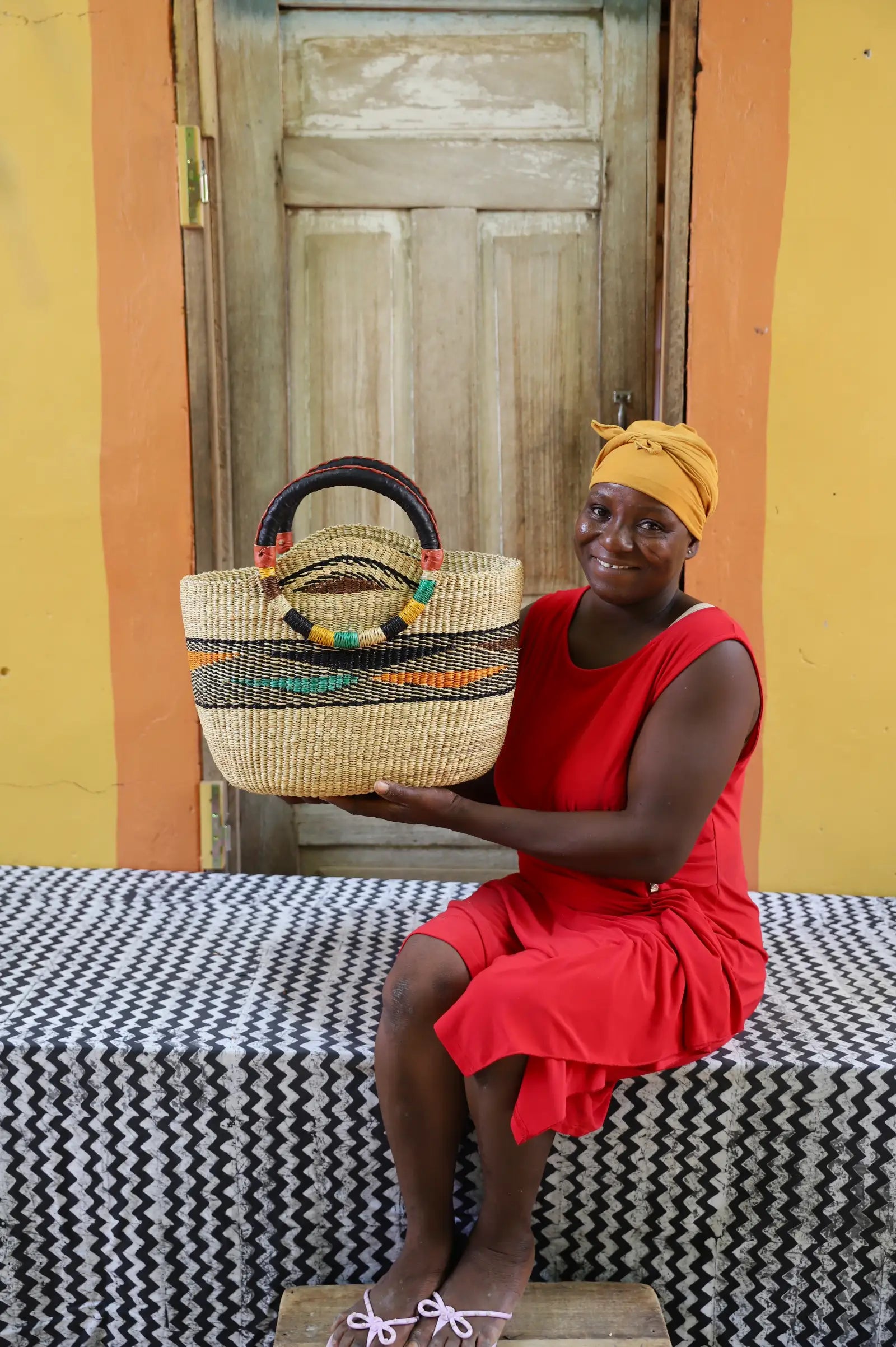 Artisan holding a colorful woven carry on bag with premium leather handles on a black and white cloth against a wooden door.