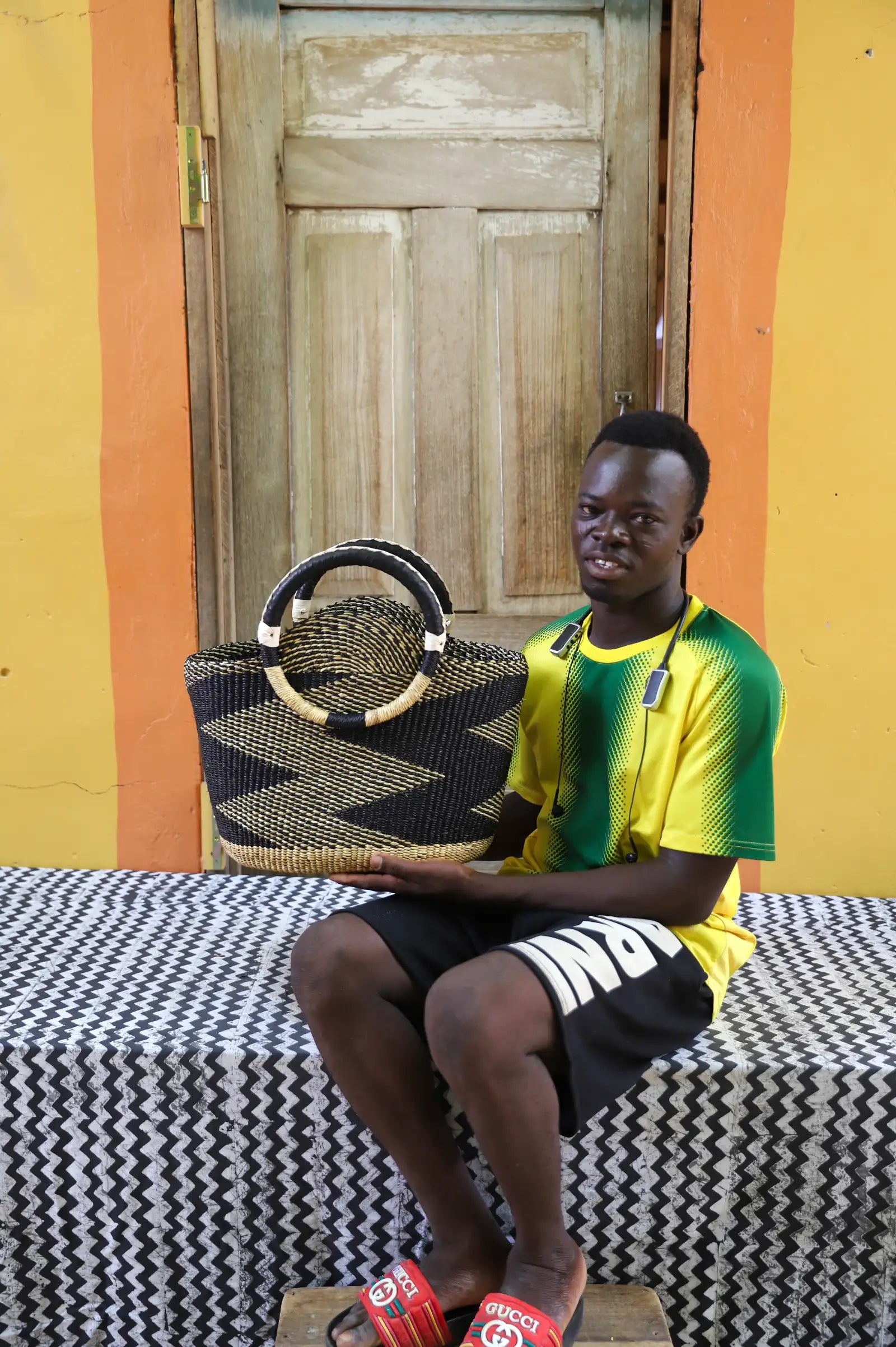 Artisan holding a colorful woven carry on bag with premium leather handles on a black and white cloth against a wooden door.