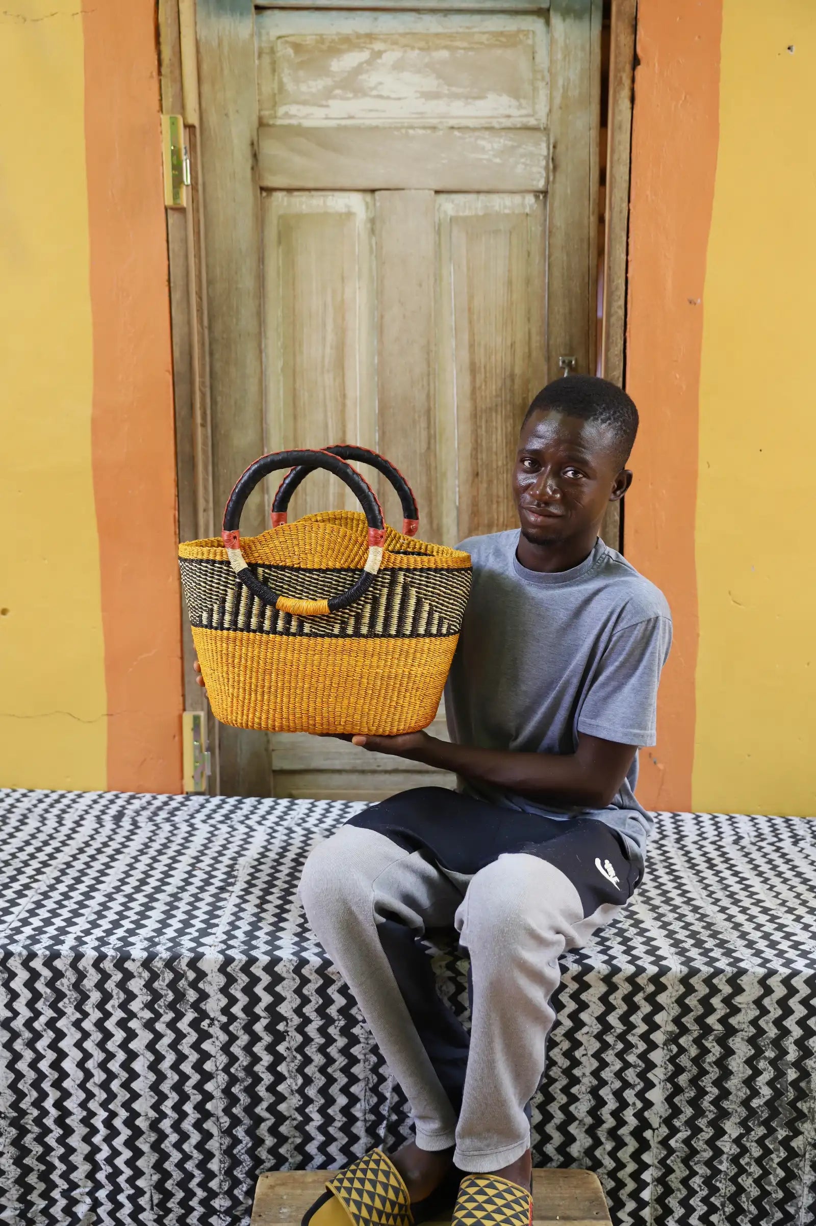 Artisan holding a colorful woven carry on bag with premium leather handles on a black and white cloth against a wooden door.