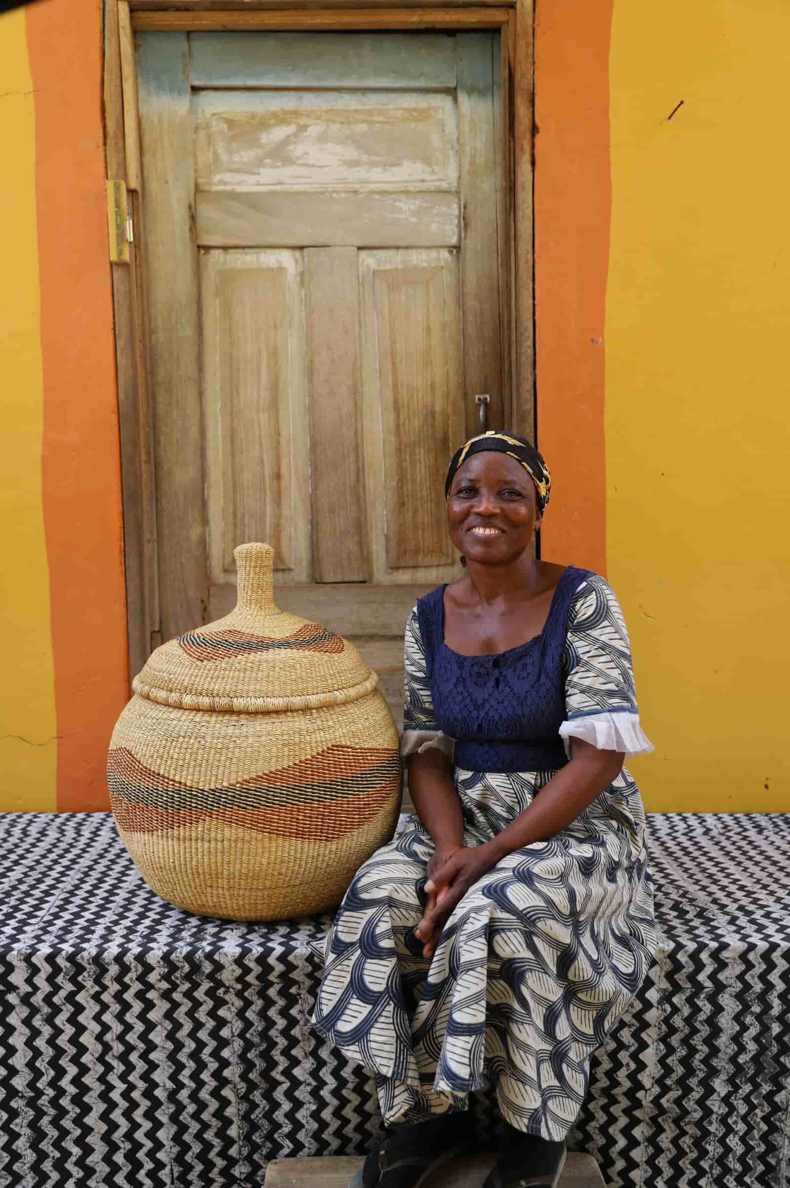 Woman seated beside large Orbit storage basket in natural straw with rust diagonal swirl