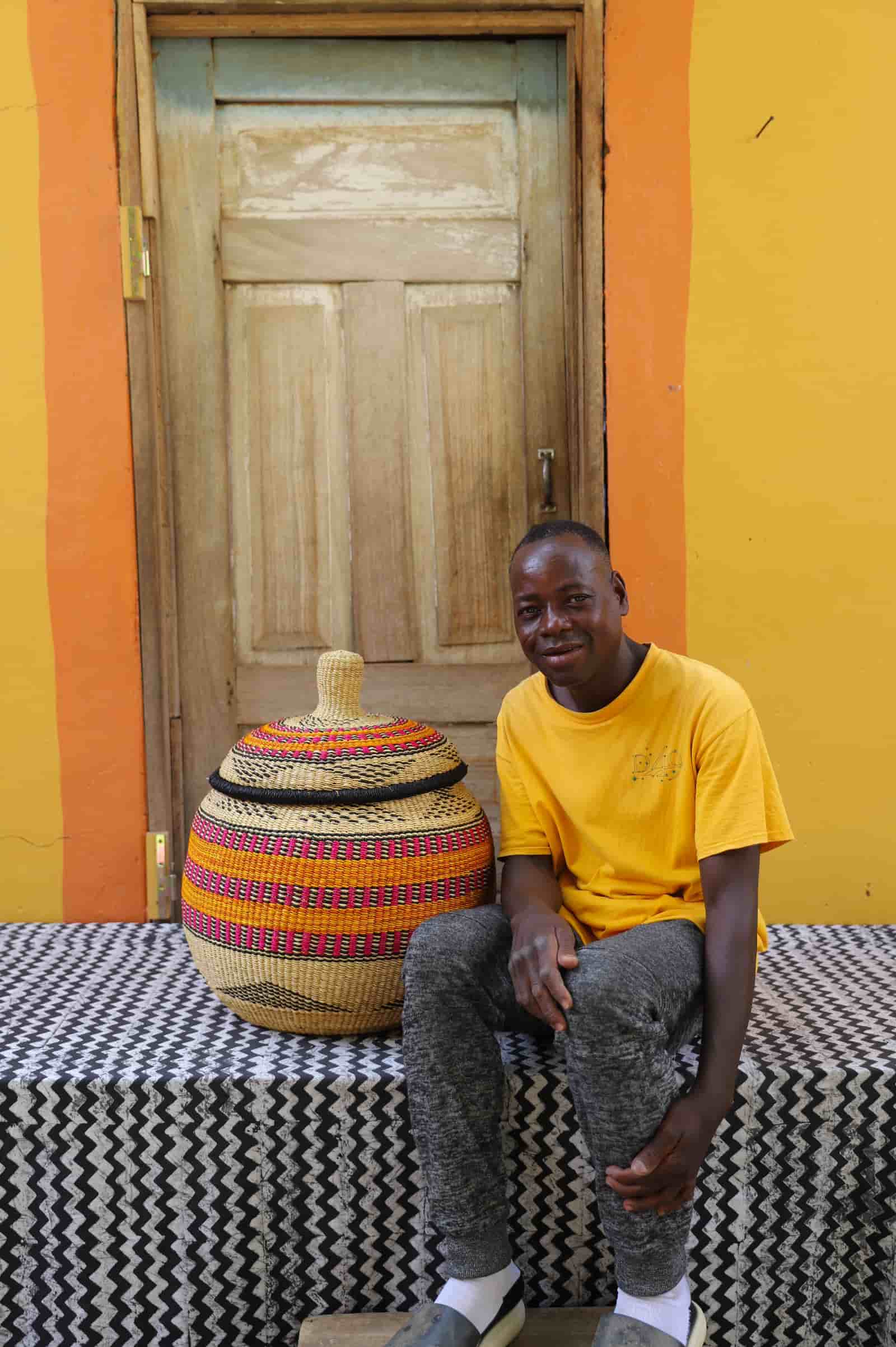 Man seated beside large Orbit storage basket in natural straw with orange and pink bands
