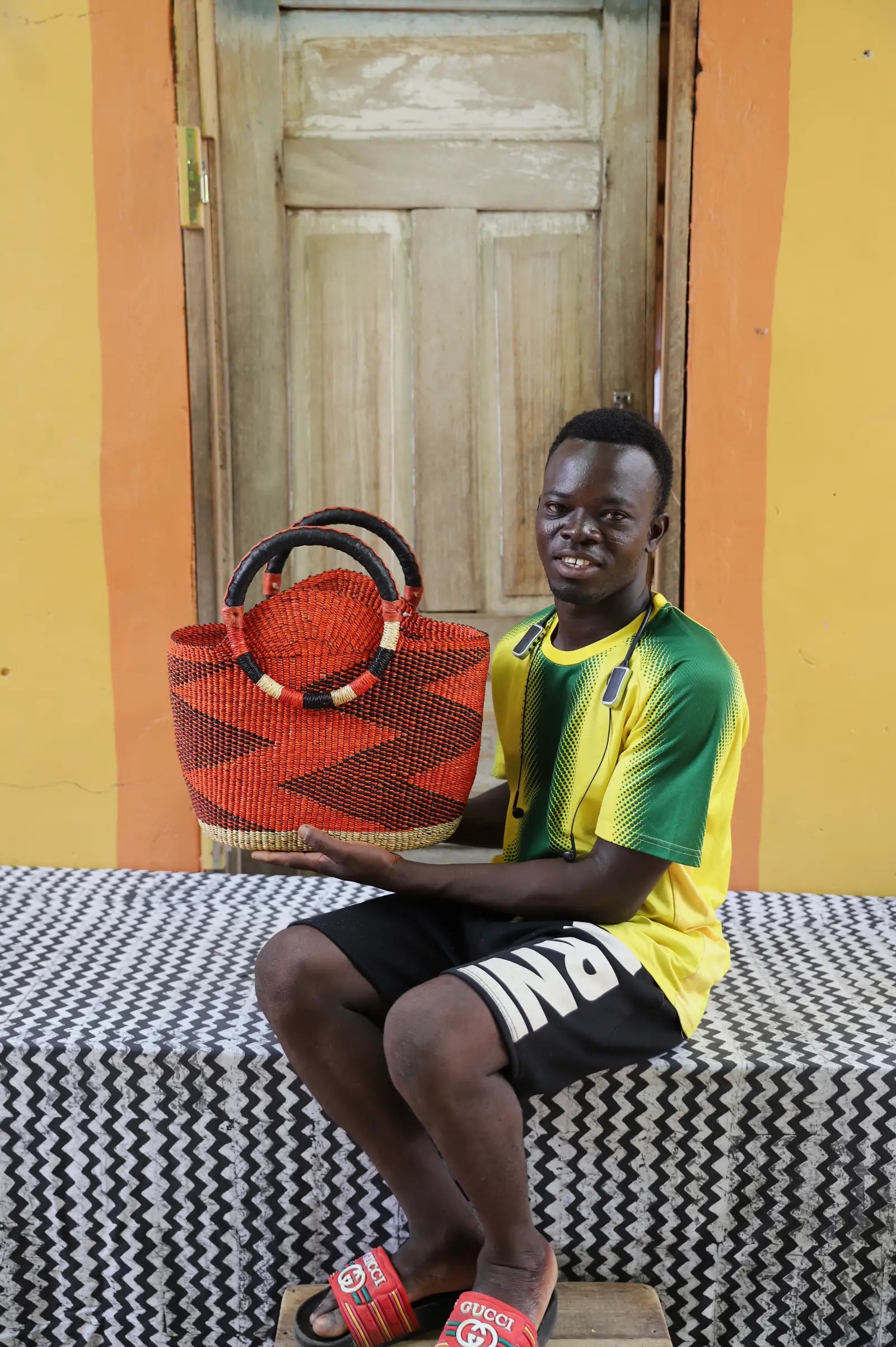Artisan holding a colorful woven carry on bag with premium leather handles on a black and white cloth against a wooden door.
