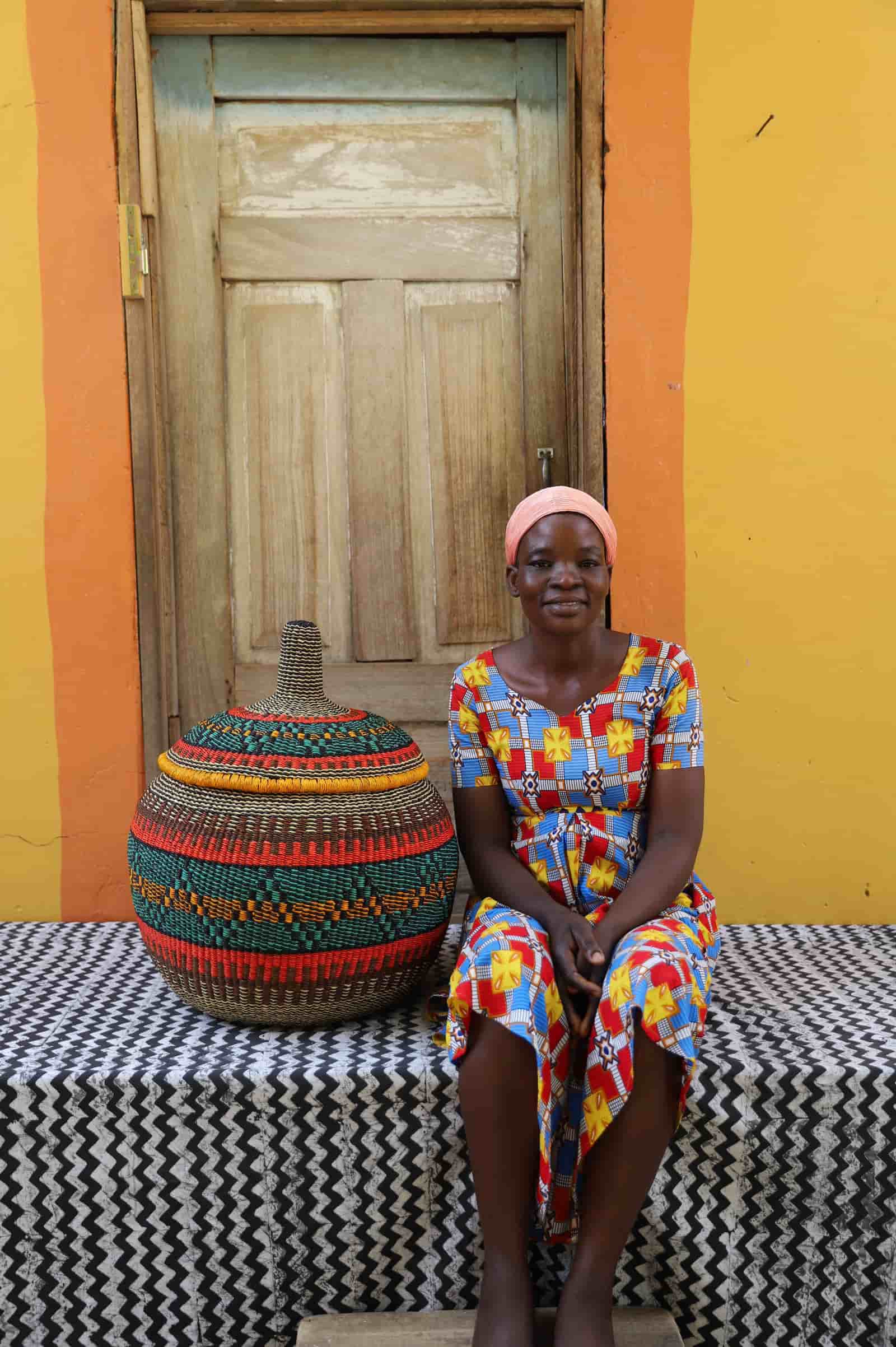 Woman seated beside large Orbit storage basket in dark teal with orange and red stripe bands