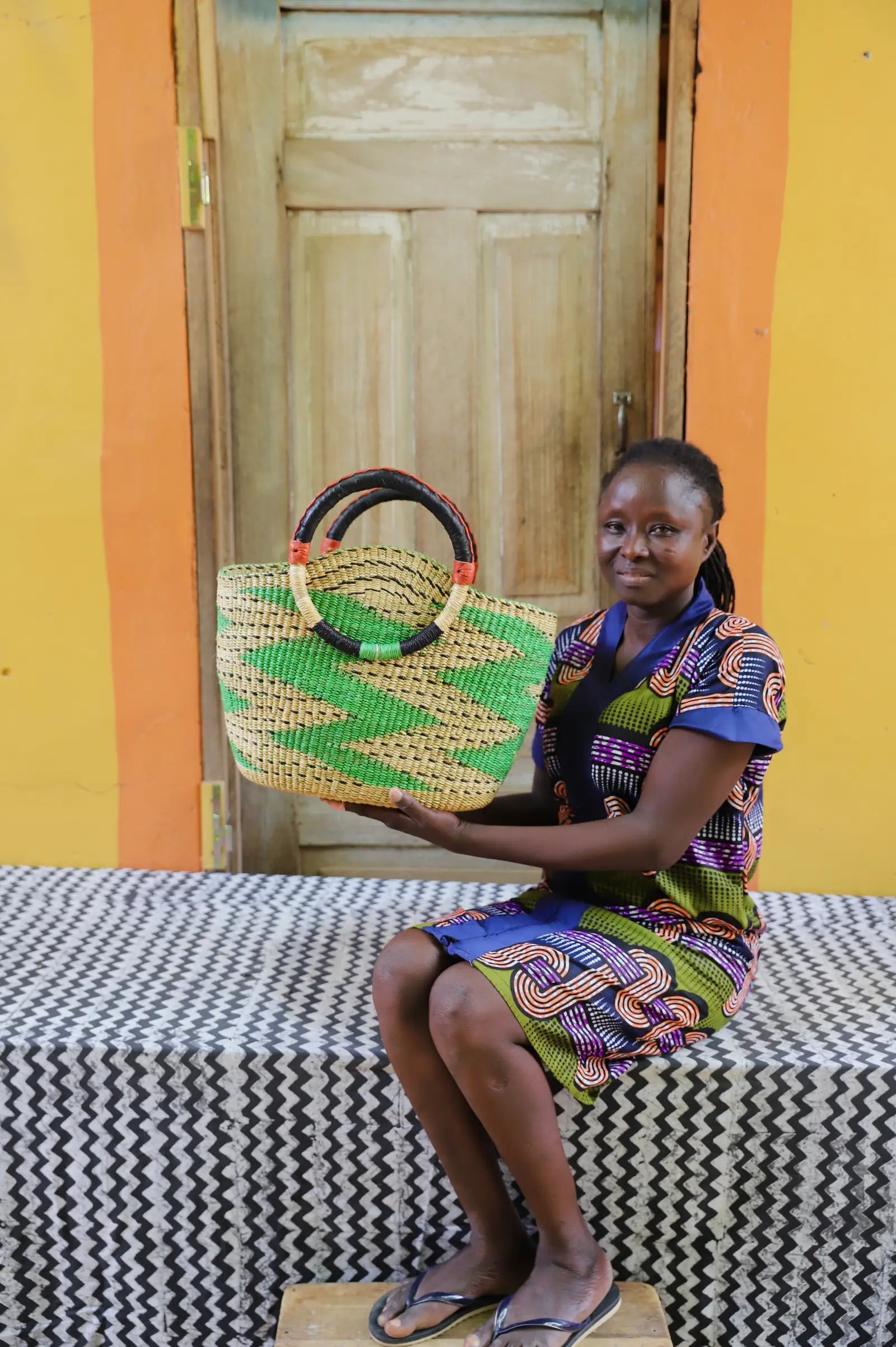 Colorful woven carry on bag with premium leather handles on a black and white cloth against a wooden door.