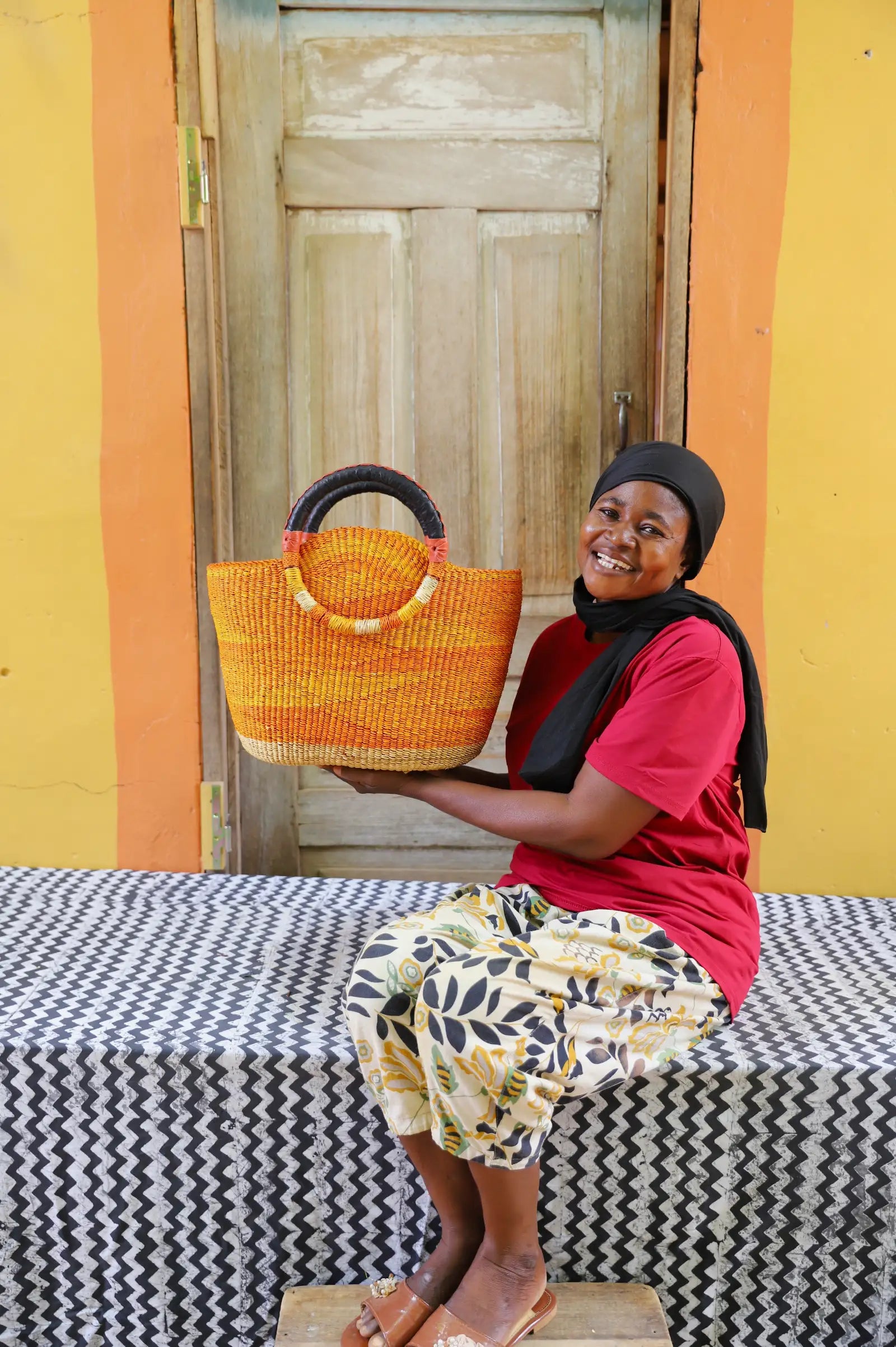Woman holding a colorful woven carry on bag with premium leather handles on a black and white cloth against a wooden door.