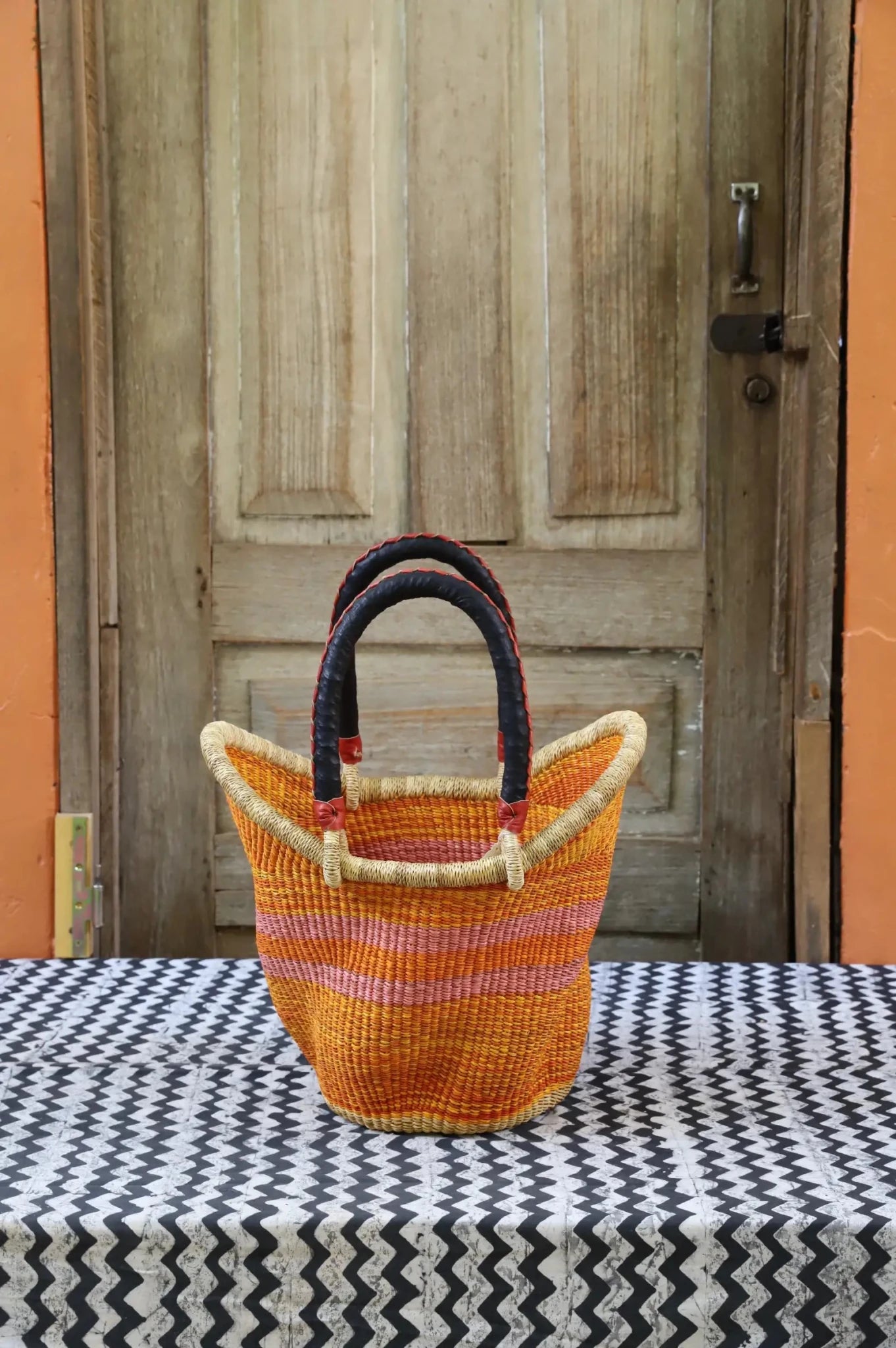Woven carry on basket with premium leather on a black and white cloth against a wooden door