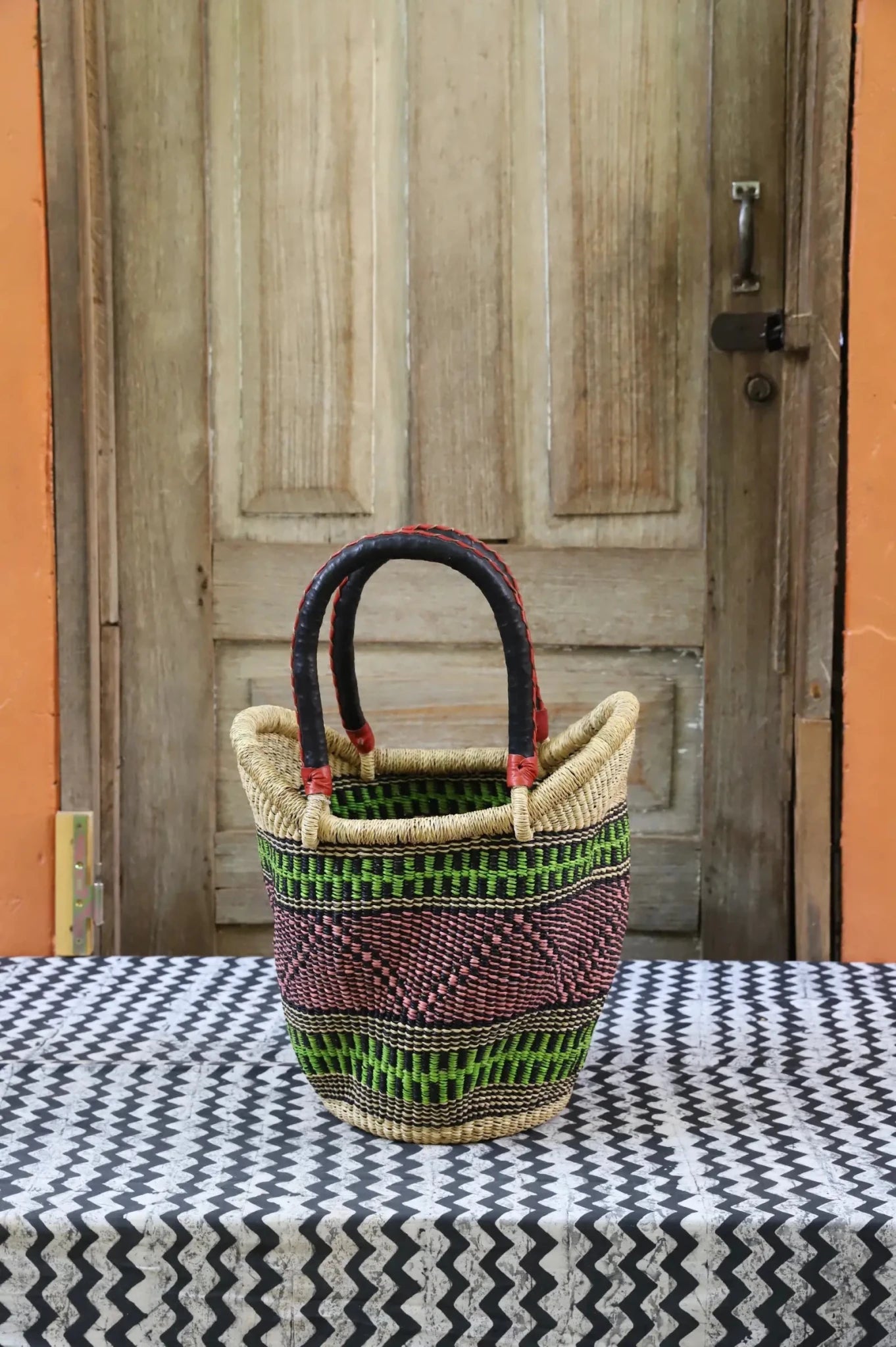 Woven carry on basket with premium leather on a black and white cloth against a wooden door