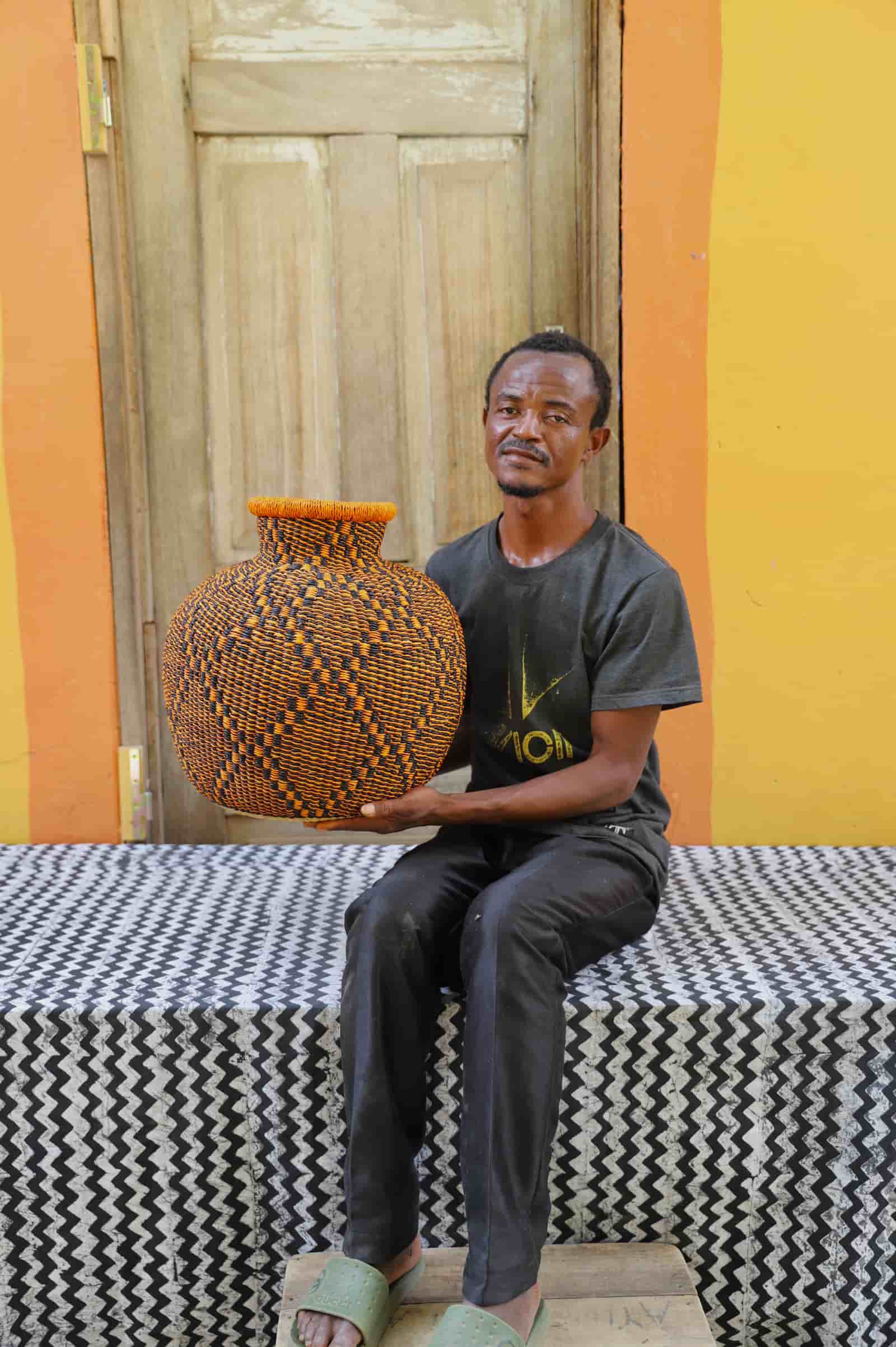 Artisan holding a colorful woven storage basket  on a black and white cloth against a wooden door.