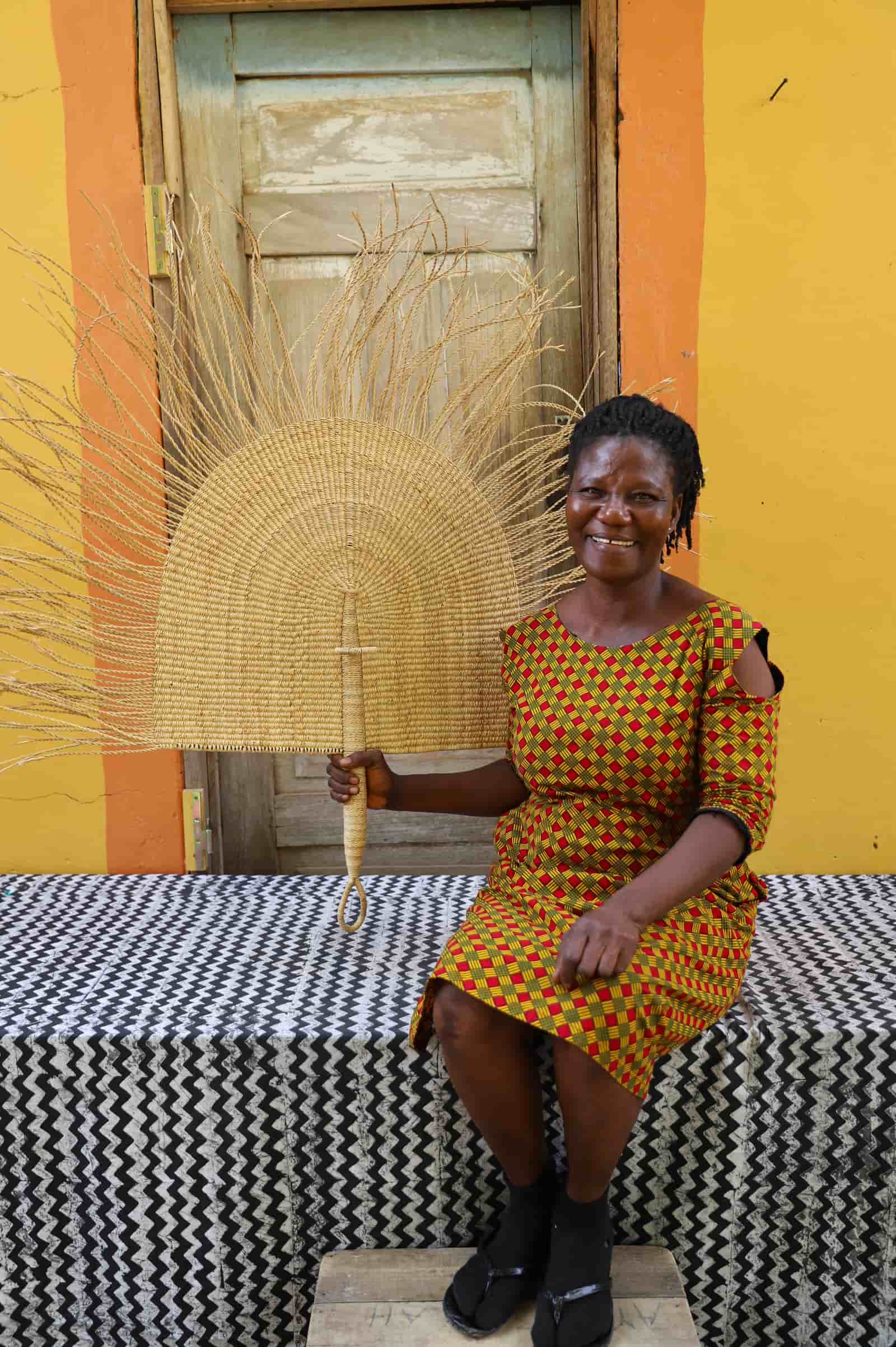 Woman holding a woven fan against a colorful wall