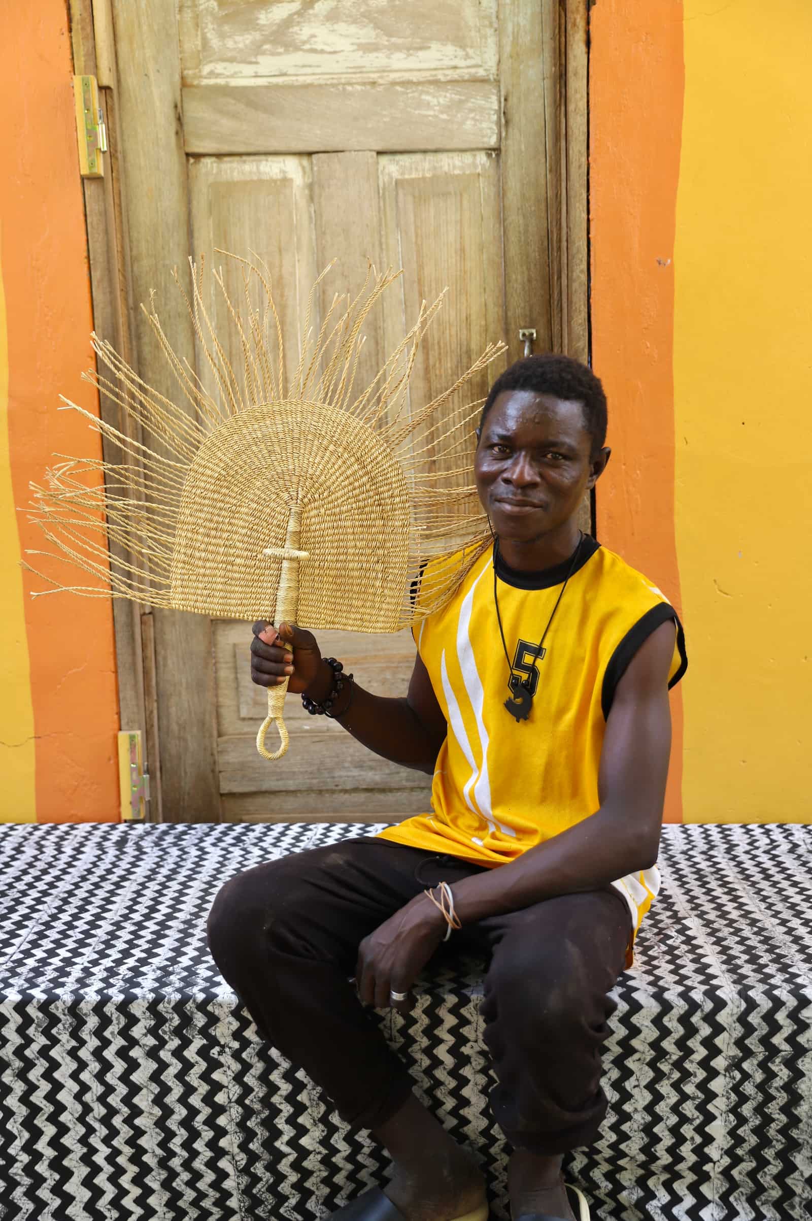 Man  holding a woven sun-shaped object against a colorful background