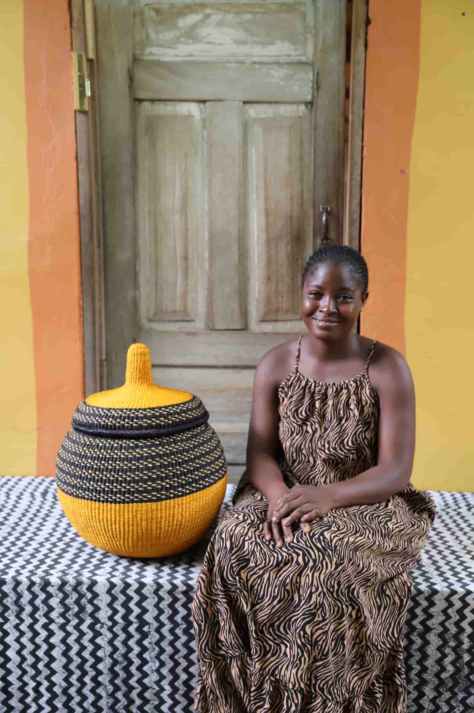 Woman seated beside large Orbit storage basket in yellow and black stripe, showing scale