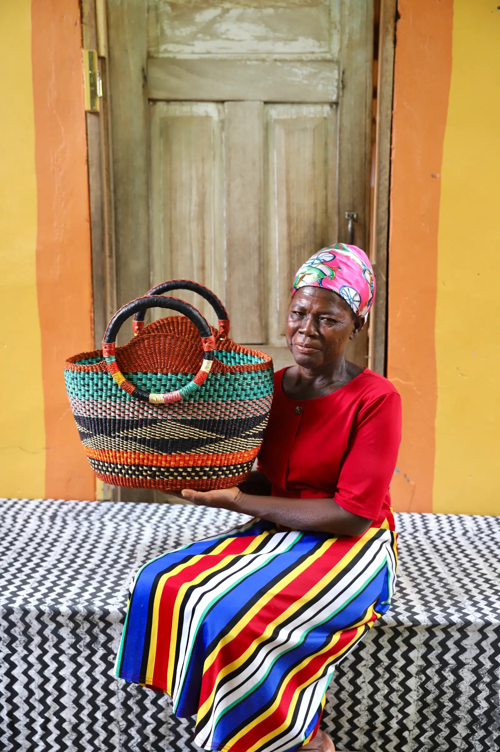 Artisan holding a colorful woven carry on bag with premium leather handles on a black and white cloth against a wooden door.
