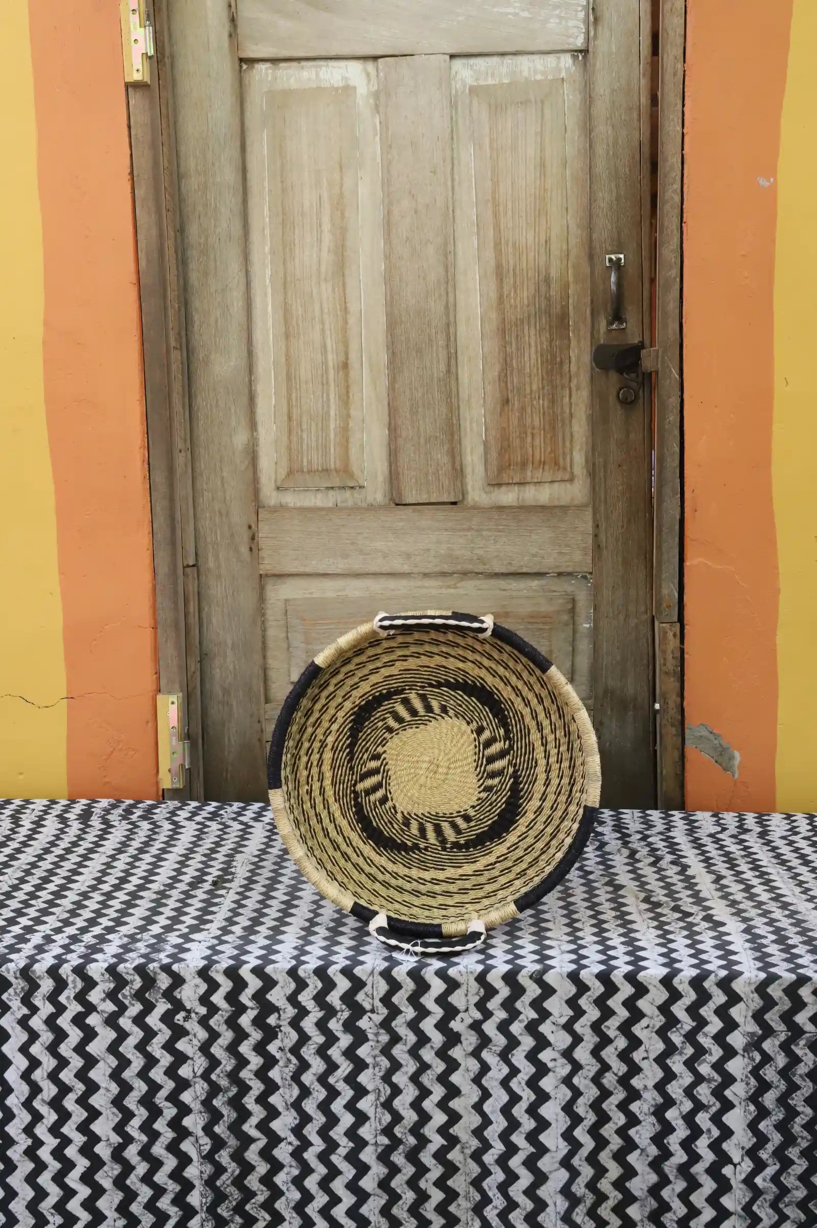 Handwoven Bolga wall tray disc in natural straw with a dark rim and yellow centre dot.